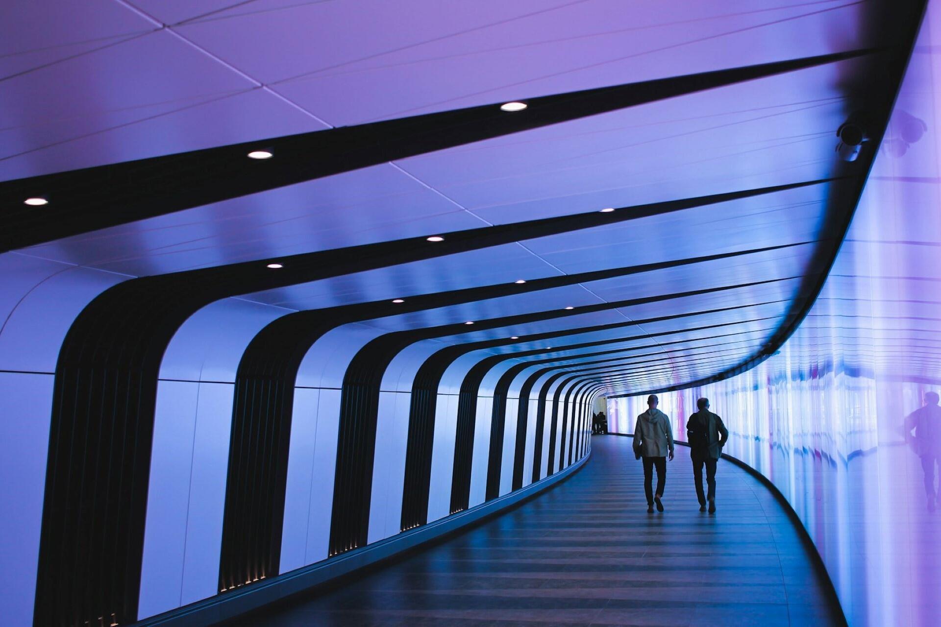 Two people walking through a modern illuminated tunnel