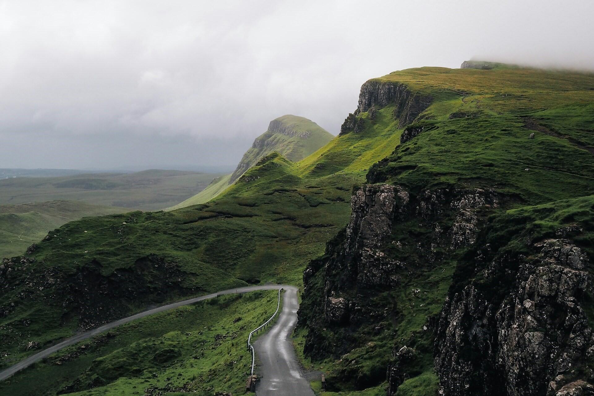 Winding road through steep green highlands and rocky cliffs in a misty Celtic landscape