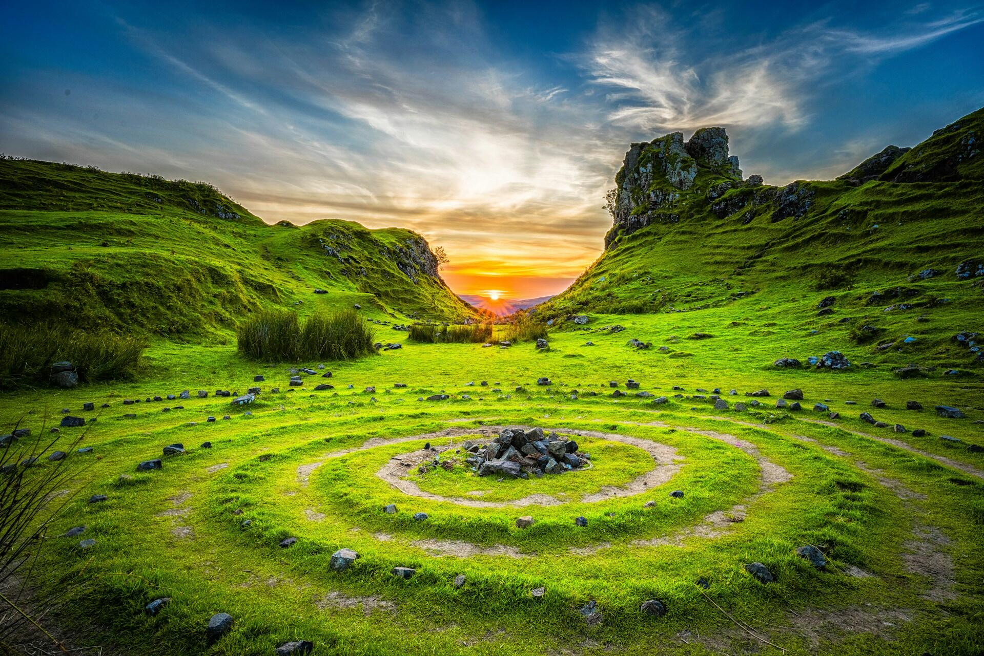 Spiral stone pattern in a grassy valley at sunset with rocky hills in the background