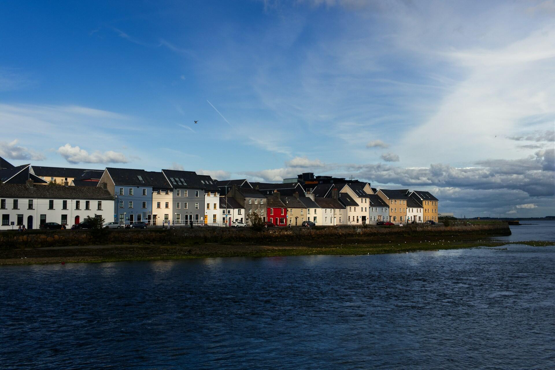 Colourful houses along a riverside in Galway, Ireland under a blue sky