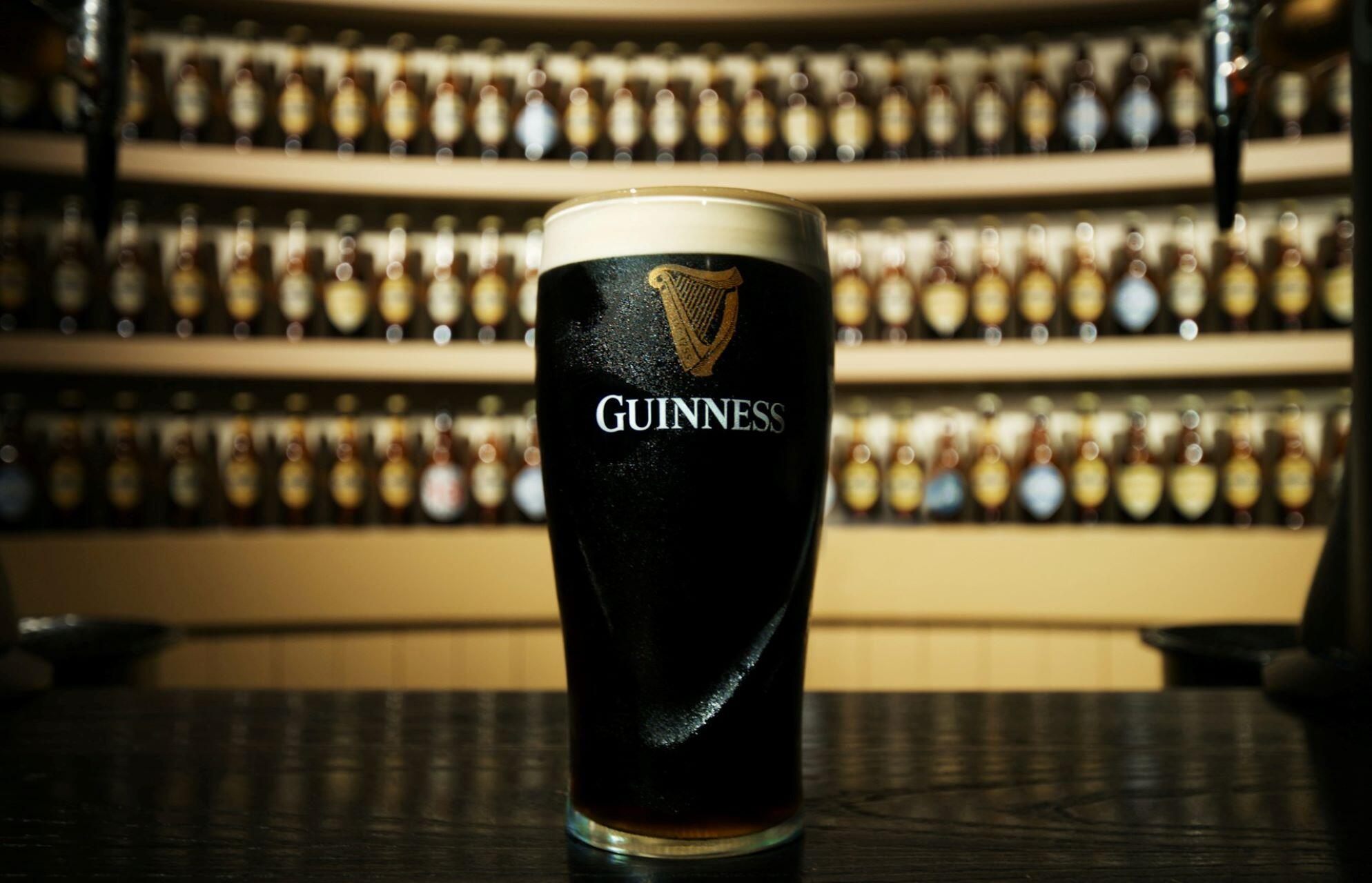 Pint of Guinness stout served in a bar with Guinness bottles in the background