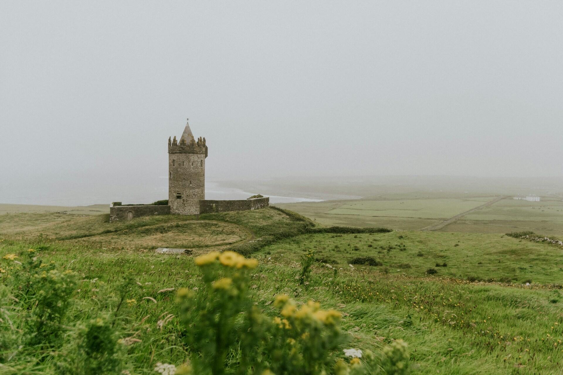 Stone tower castle on a grassy hill overlooking the Irish countryside in misty weather