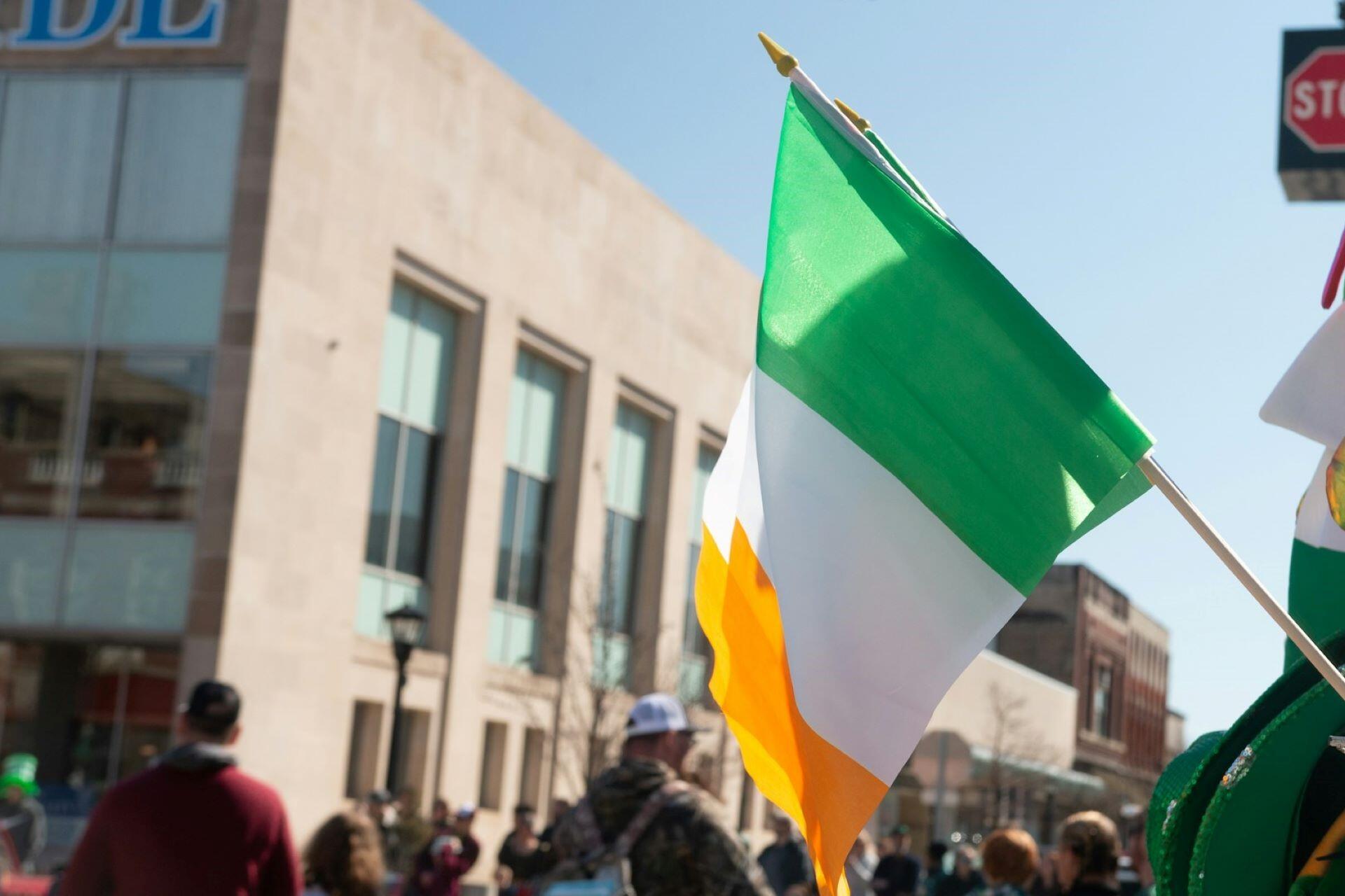 Irish tricolour flag being carried through a city street during a public celebration with people in the background