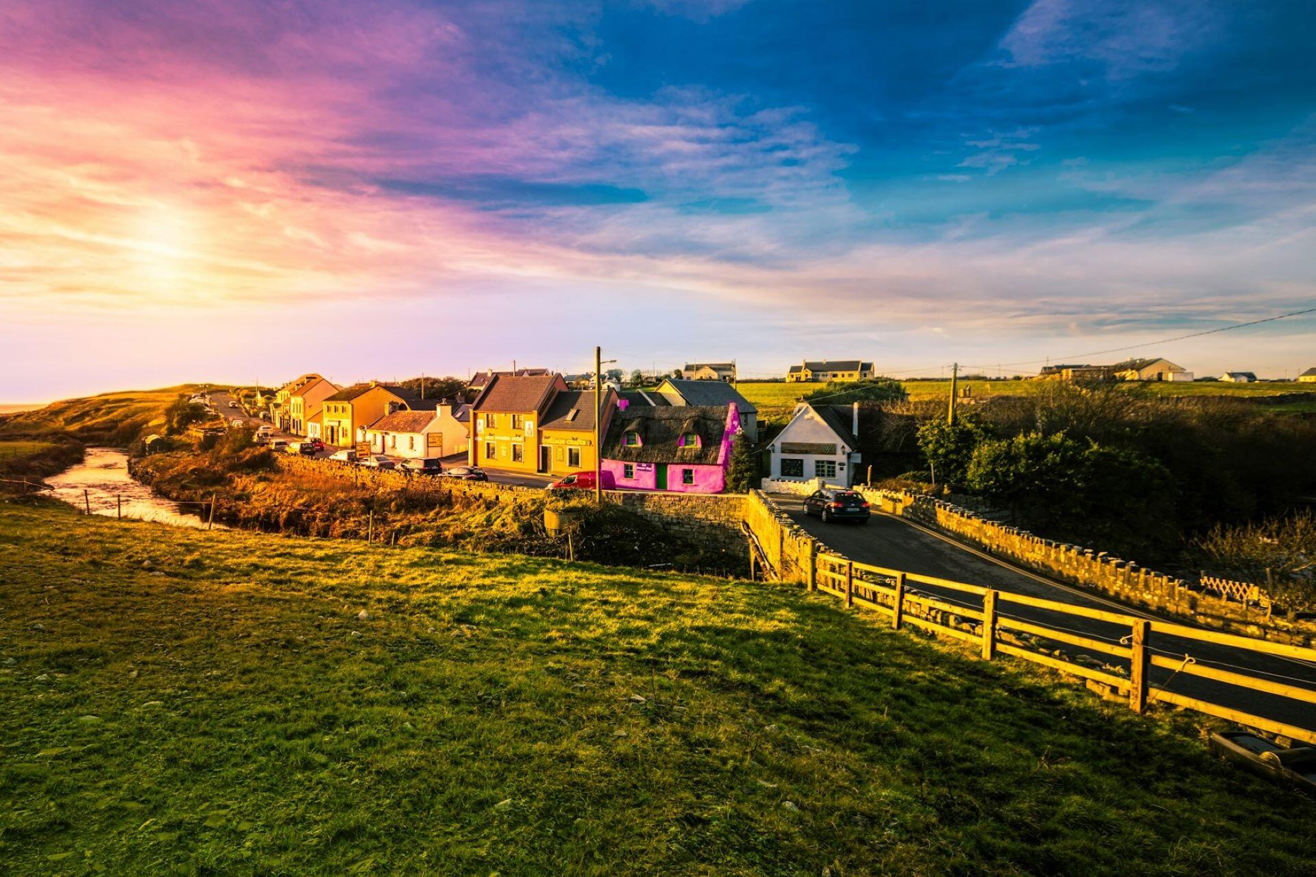 Colourful Irish village with coastal houses and countryside landscape at sunset