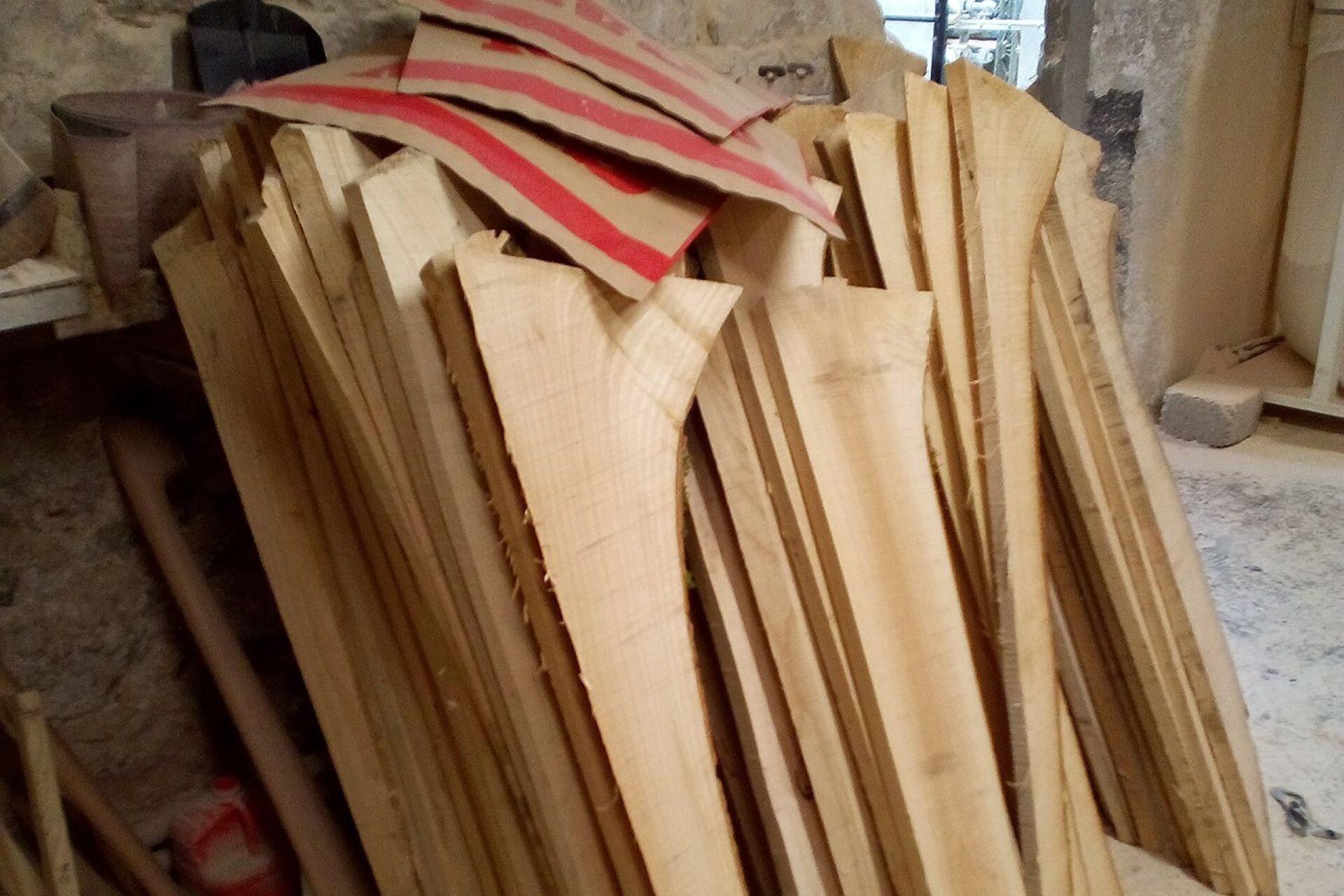 Stacks of roughly cut wooden hurley blanks leaning against a stone workshop wall.