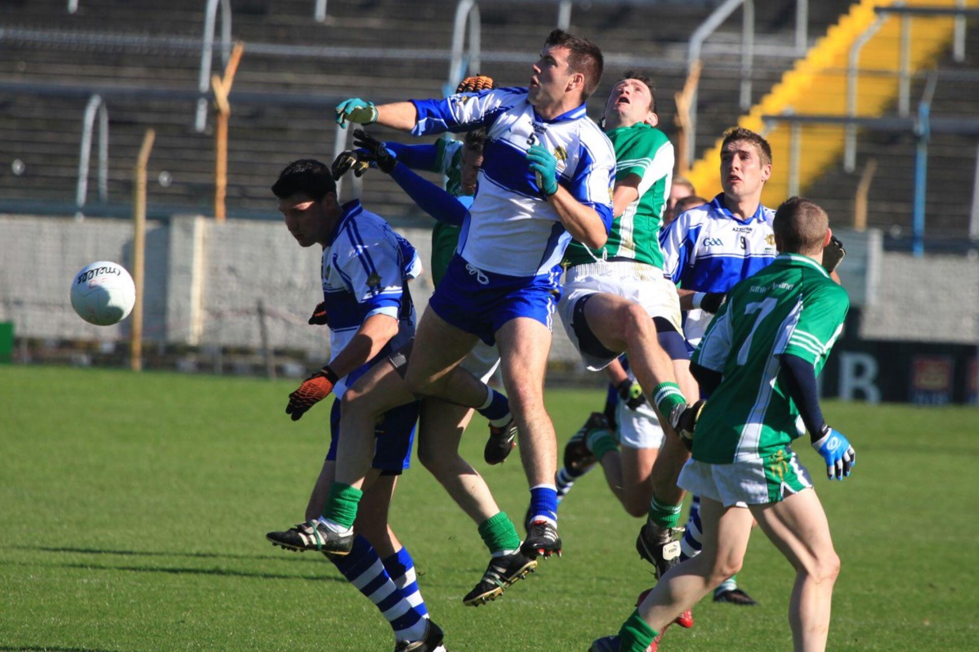 Several Gaelic football players jumping during an aerial contest as the ball travels nearby