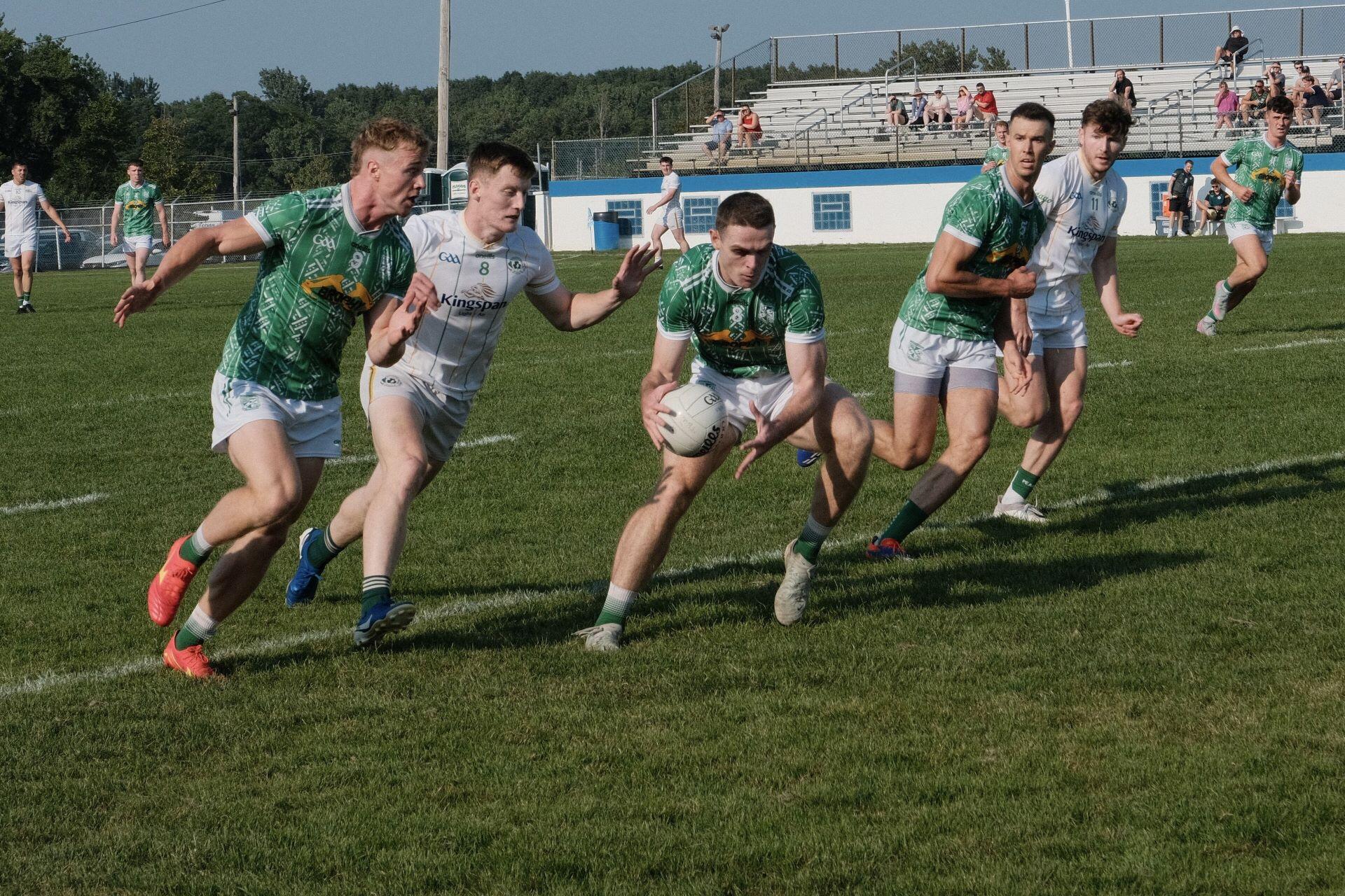 Gaelic football player carrying the ball while opponents chase him across a grass pitch