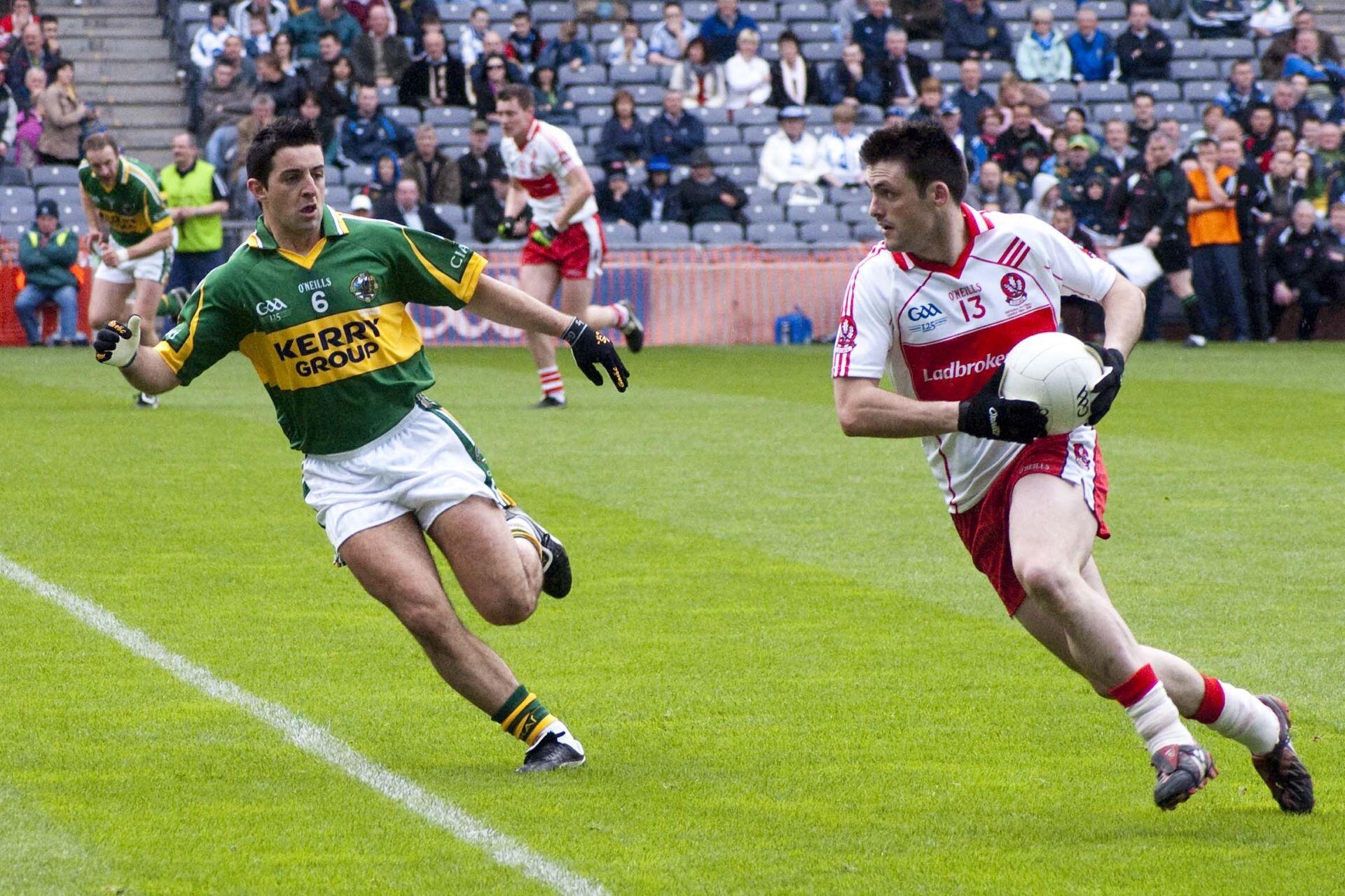 Gaelic football player carrying the ball while an opponent closes in