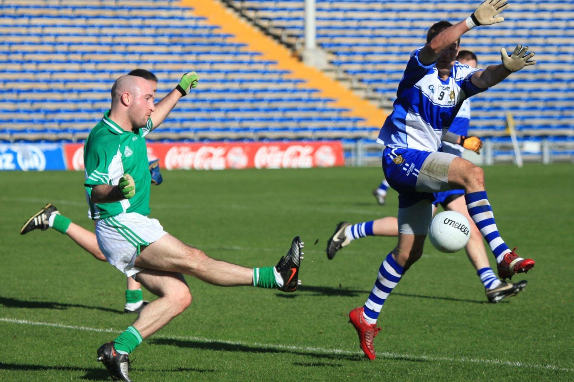 Gaelic football player kicking the ball as an opponent raises both arms to block him