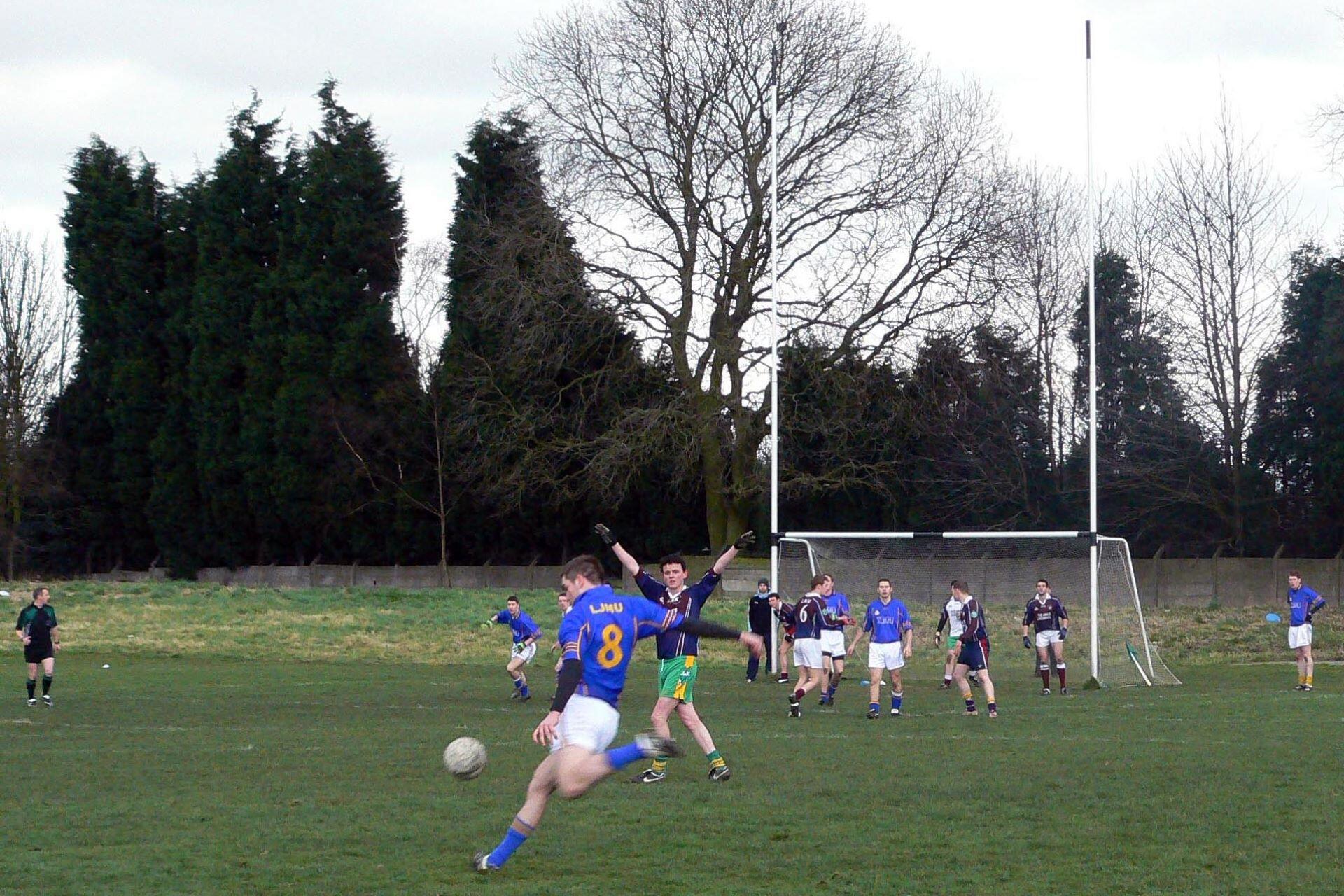 Gaelic football player kicking the ball towards goal as defenders stand near the posts