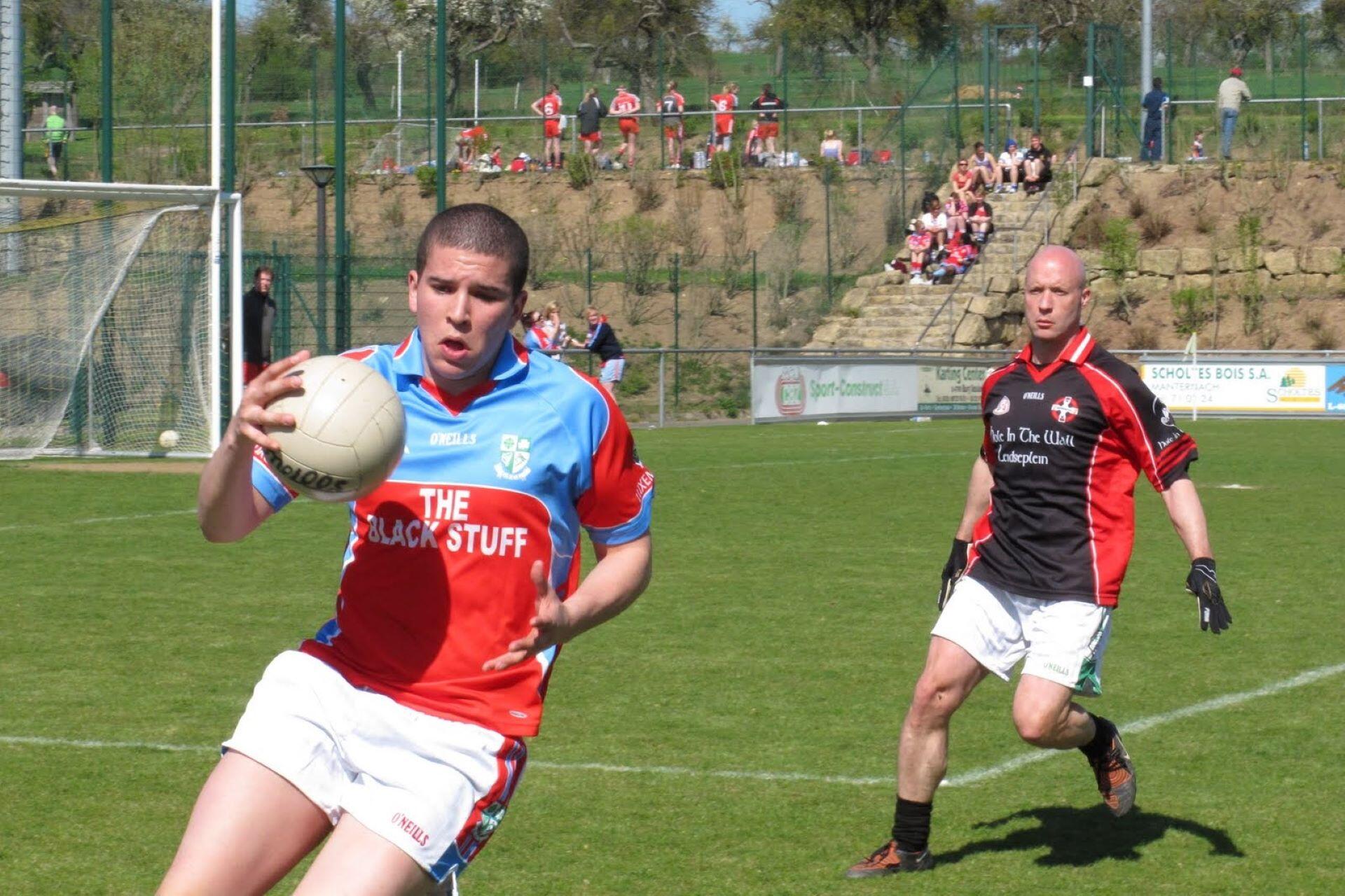 Gaelic football player running with the ball as a defender follows