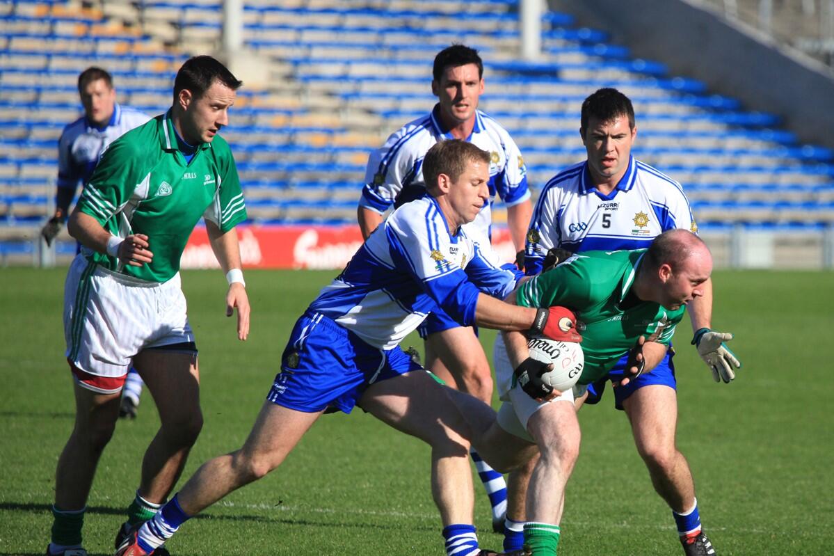 Gaelic football player holding the ball while two opponents challenge him