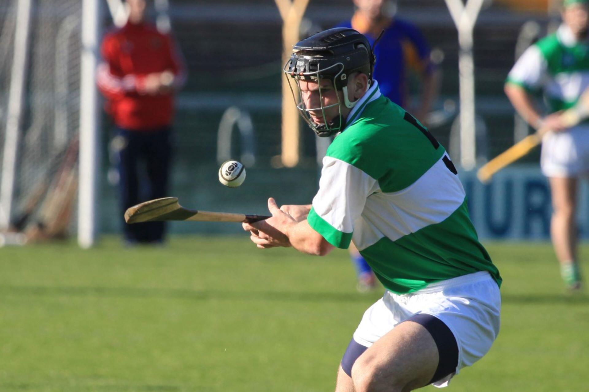 Hurling player in a green and white jersey controlling a sliotar with his hurley