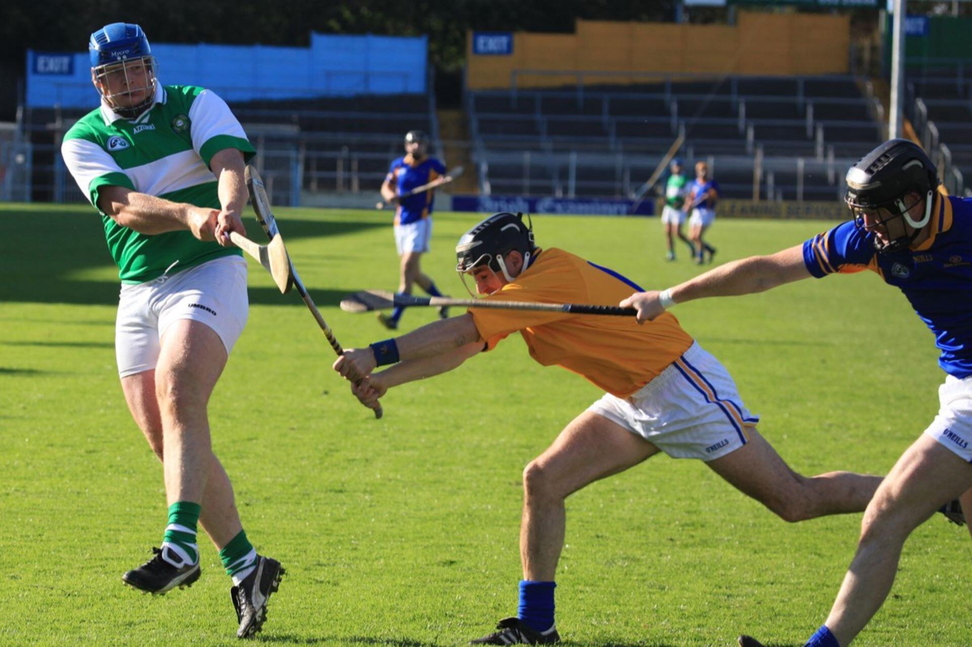 Three hurling players reaching with their hurleys as one player strikes the sliotar