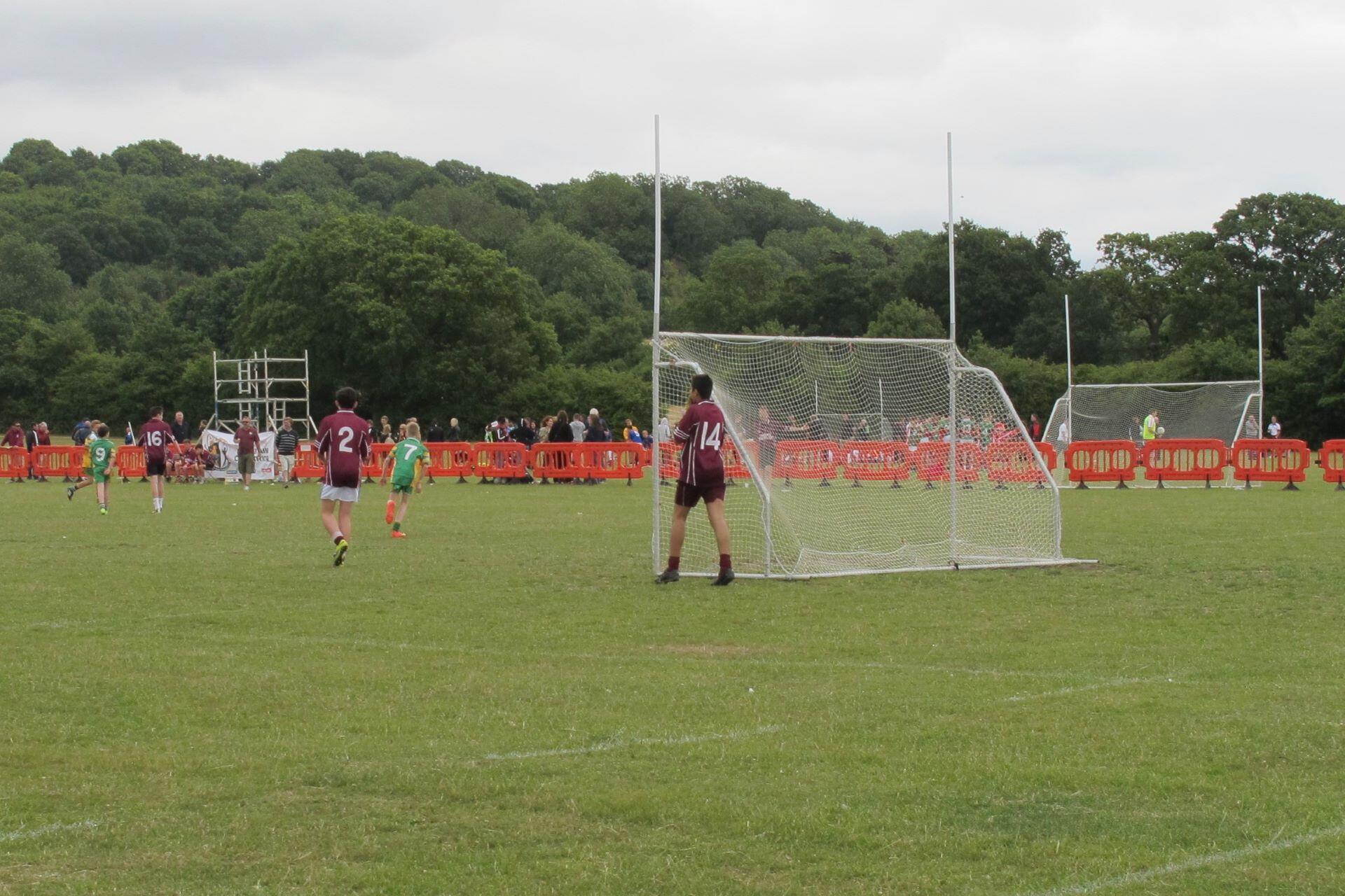 Young Gaelic football players positioned around a goal on a grass playing field