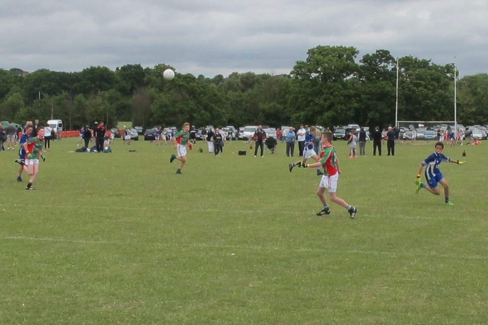 Young Gaelic football players running across a grass pitch as the ball travels through the air
