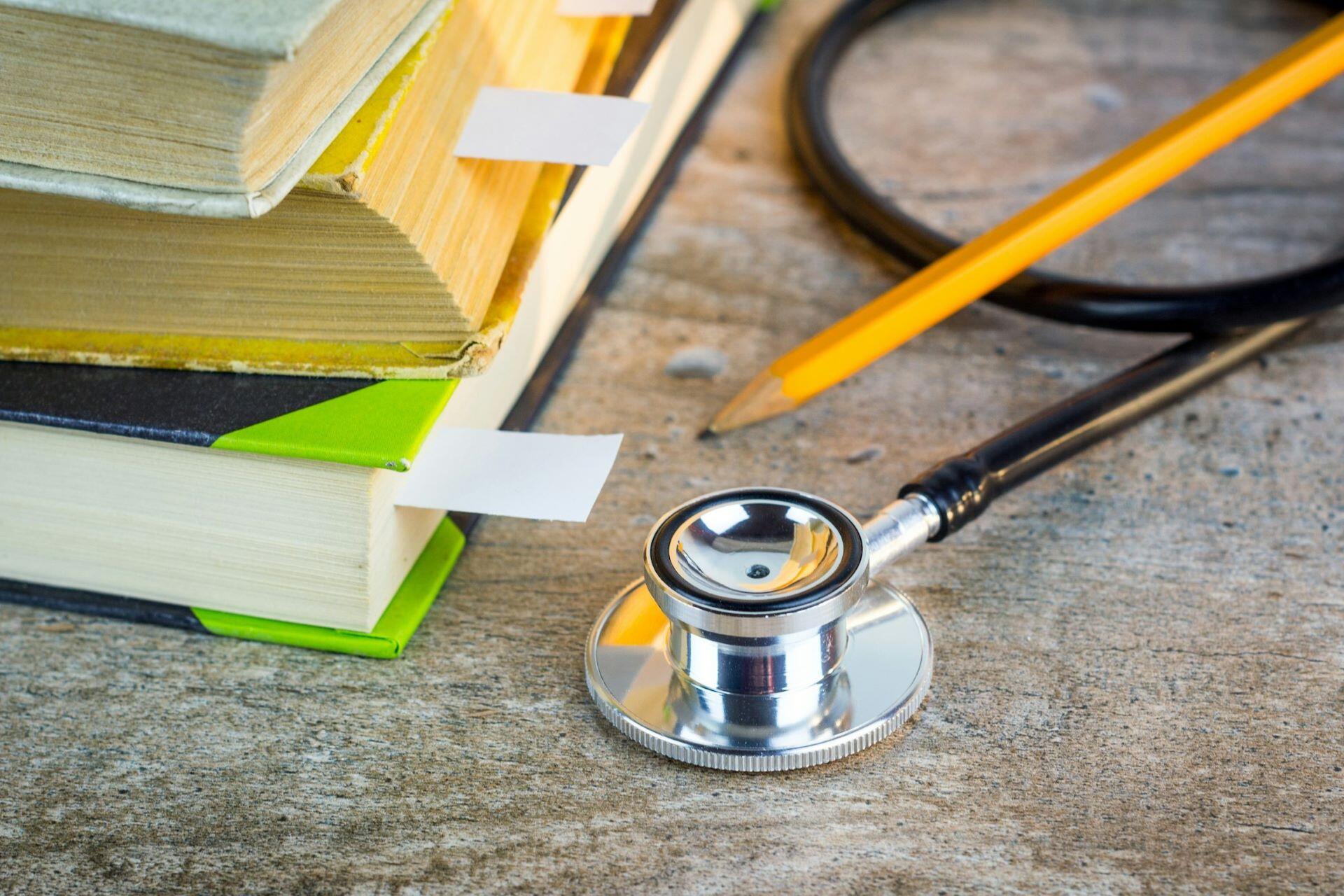 Stethoscope beside a stack of books and a pencil