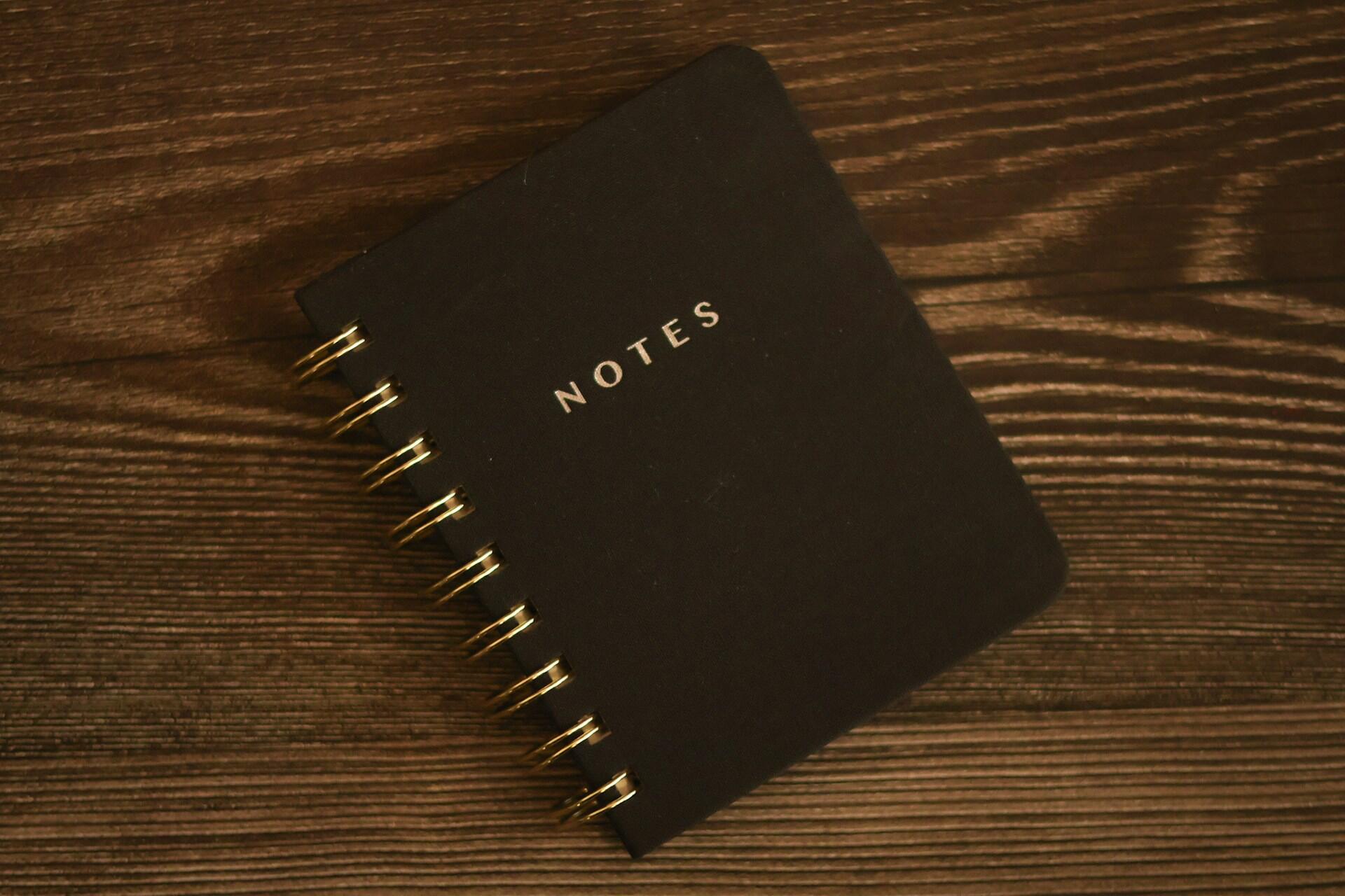 Black spiral notebook labelled “Notes” on a wooden table