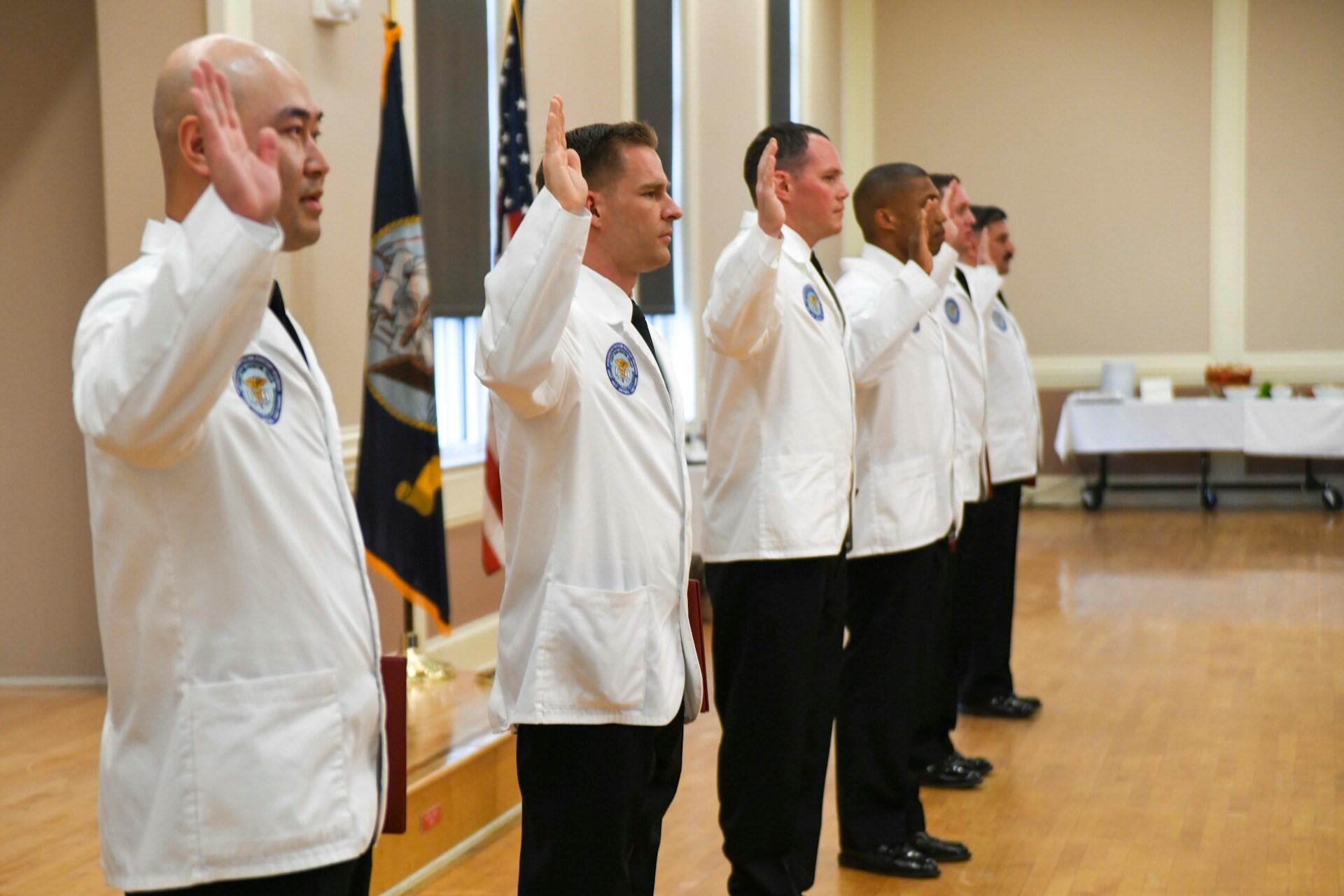People in white coats raising their right hands during a ceremony