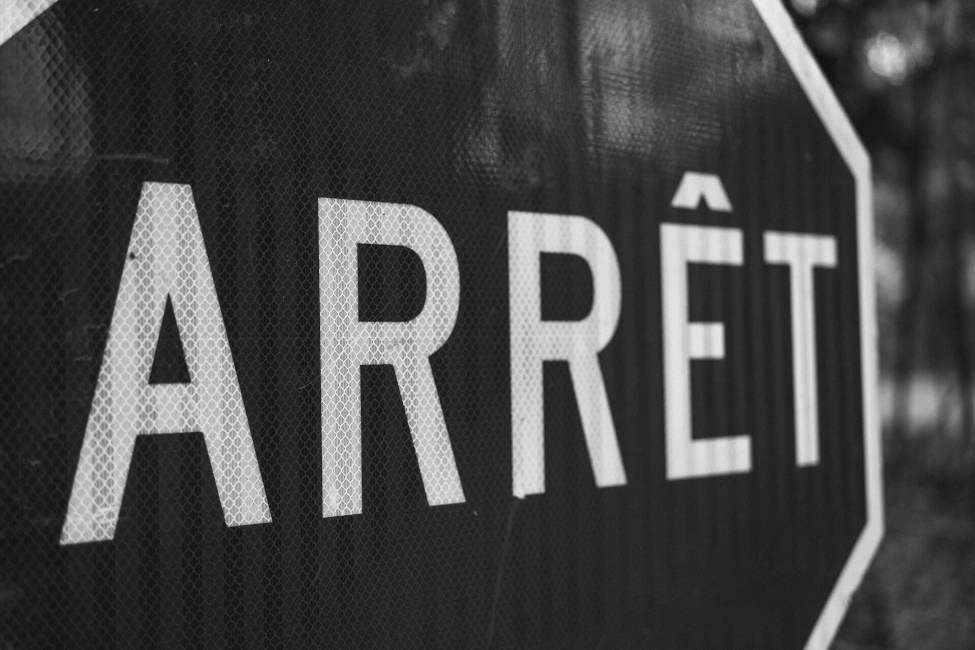 תקריב של שלט עצור שחור עם המילה "ARRÊT" מוצגת באופן בולט באותיות לבנות גדולות