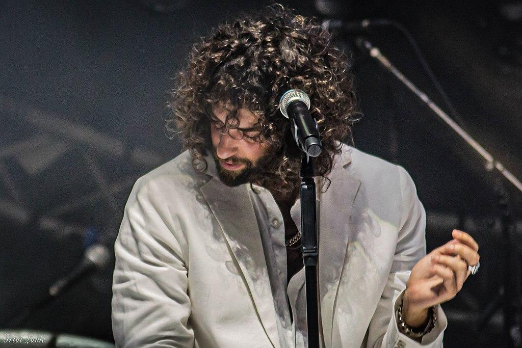 גבר מתולתל על במה מול מיקרופון