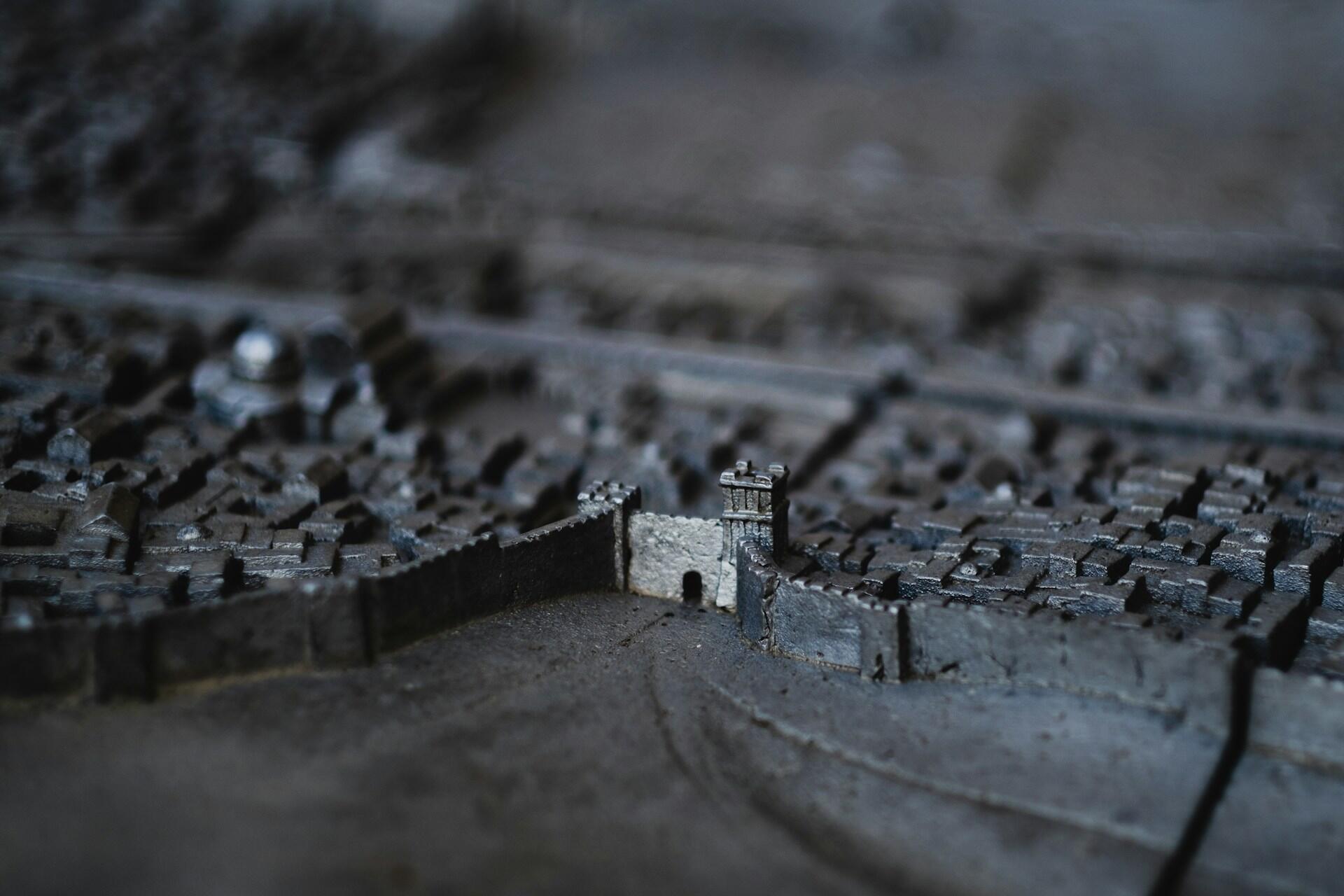 תקריב מפורט של דגם מיניאטורי המתאר עיר עתיקה עם חומות אבן ומגדלים, המציג מאפיינים אדריכליים מורכבים