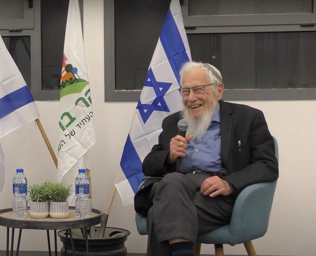 גבר מבוגר יושב על כיסא ואוחז במיקרופון