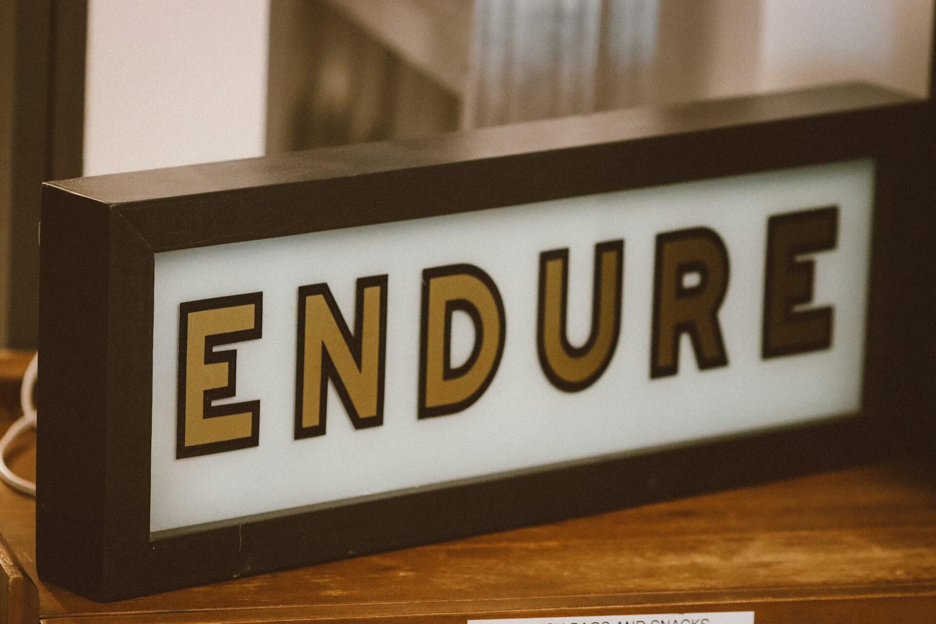 תיבת אור על משטח עץ המציגה את המילה "ENDURE" באותיות חומות מודגשות עם גבול שחור