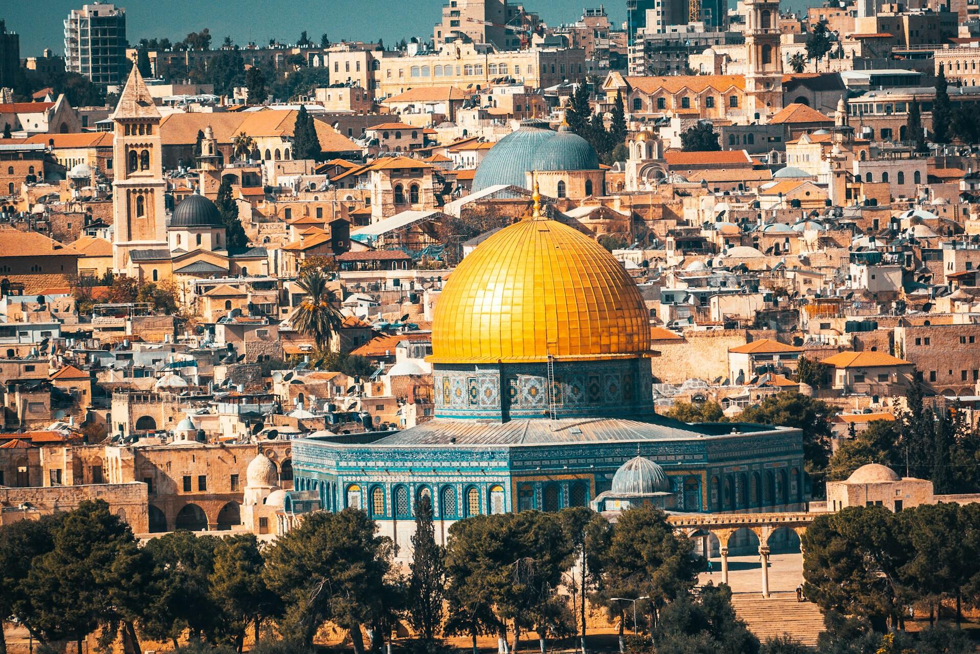 נוף של כיפת הסלע עם כיפת הזהב שלה, מוקפת עצים ומבנים היסטוריים בנוף העירוני של ירושלים