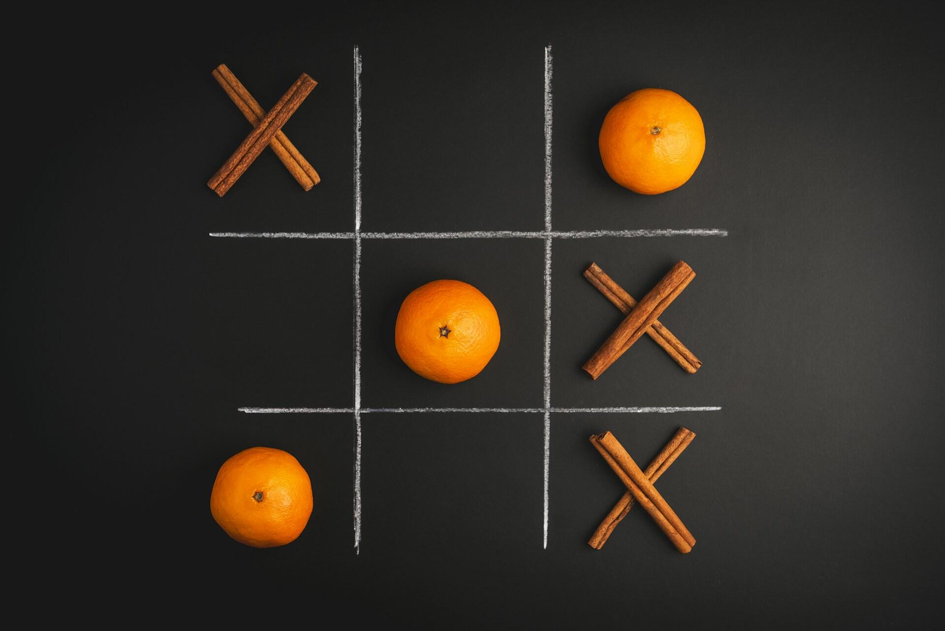 משחק איקס-עיגול המצויר על משטח שחור, ובו תפוזים כ-"O" ומקלות קינמון כ-"X"