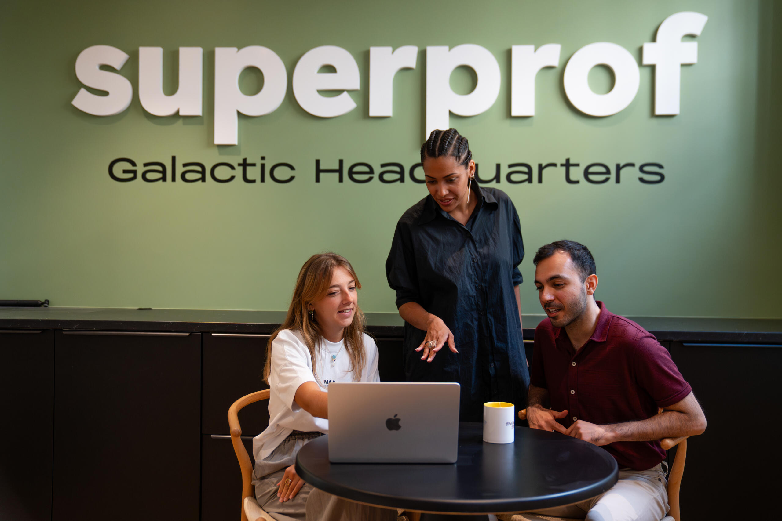 שלושה אנשים מנהלים דיון סביב מחשב נייד ליד שולחן בחדר שעליו מתנוסס הכיתוב