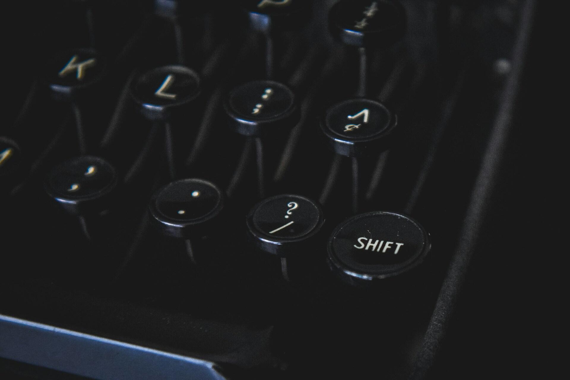 תקריב של מקשי מכונת כתיבה וינטג' הכוללים "SHIFT" וסימני פיסוק על מקשים עגולים שחורים