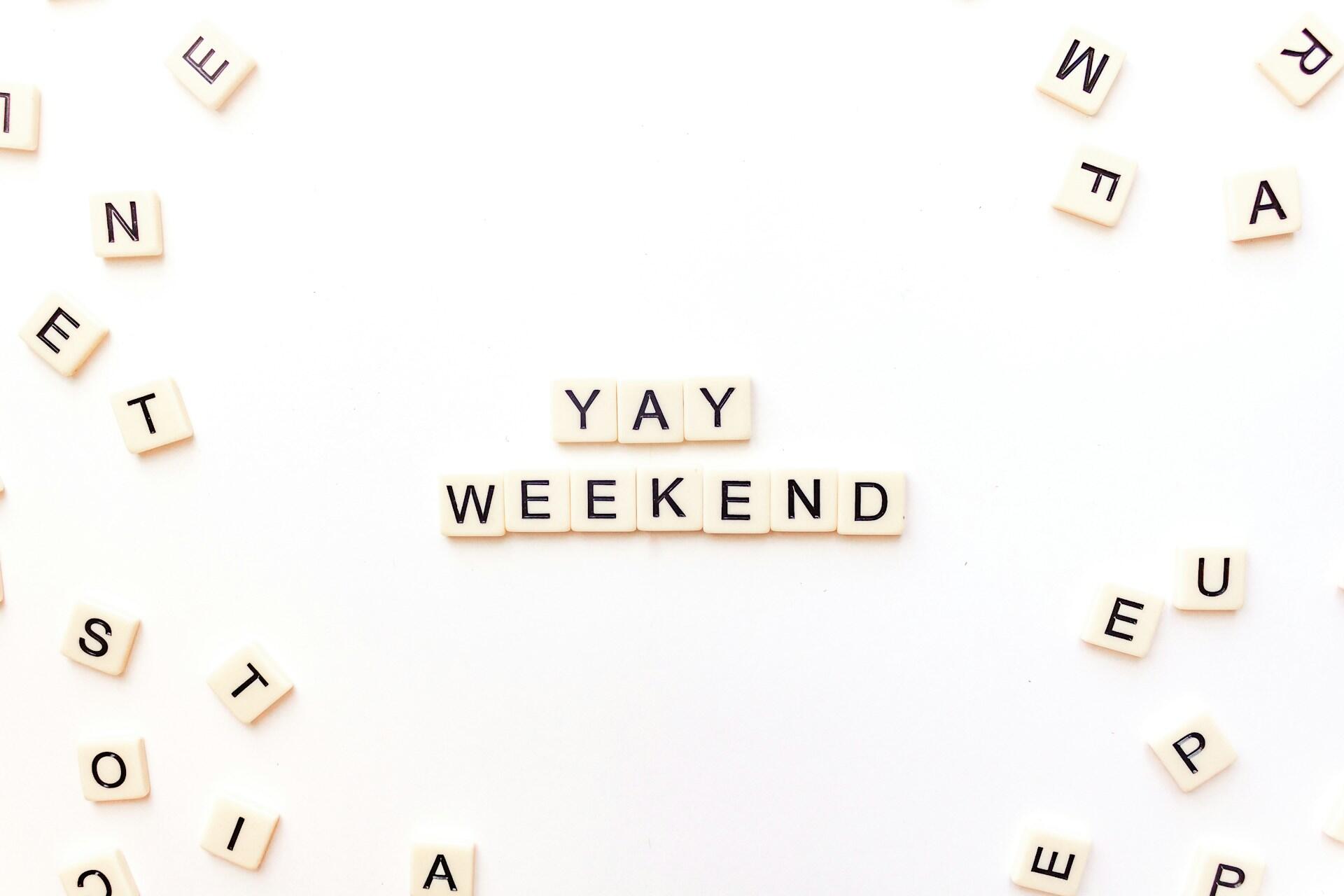 אריחי סקראבל על רקע לבן מאייתים "YAY WEEKEND" מוקפים באריחי אותיות פזורים