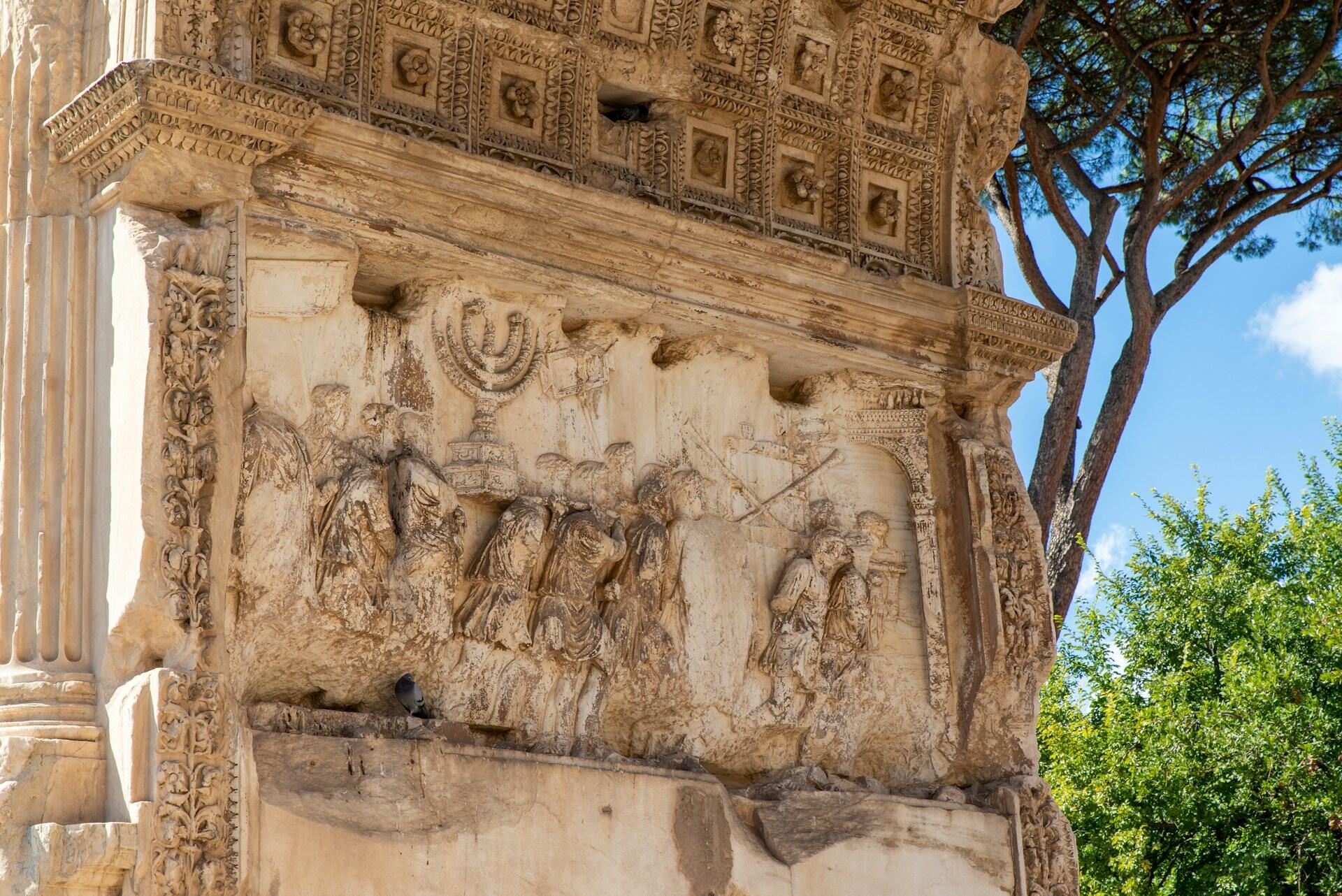 תבליט אבן מפורט על קשת רומית עתיקה המתאר חיילים הנושאים חנוכייה ושלל אחר, עם גילופים אדריכליים מעוטרים מעל