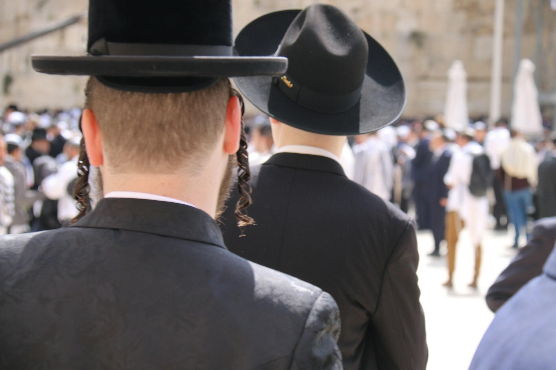 גברים חובשים כובעים וחליפות שחורים מסורתיים בכינוס דתי צפוף, במבט מאחור