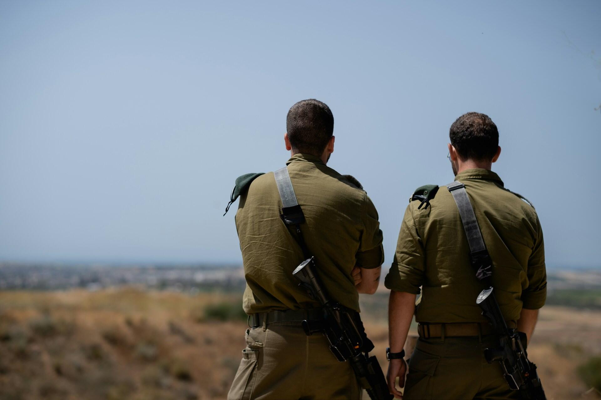 שני חיילים במדים ירוקים עם רובים עומדים ומשקיפים על נוף רחוק תחת שמיים כחולים וצלולים