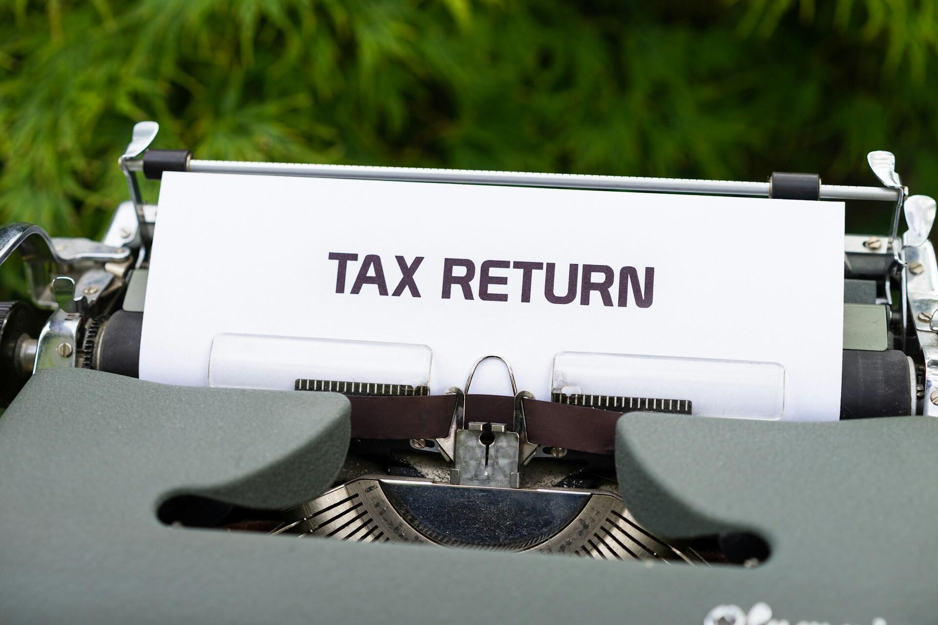 מדפסת עם נייר עליו כתוב באנגלית tax return (החזר מס) על רקע הבחוץ עם עלים ירוקים