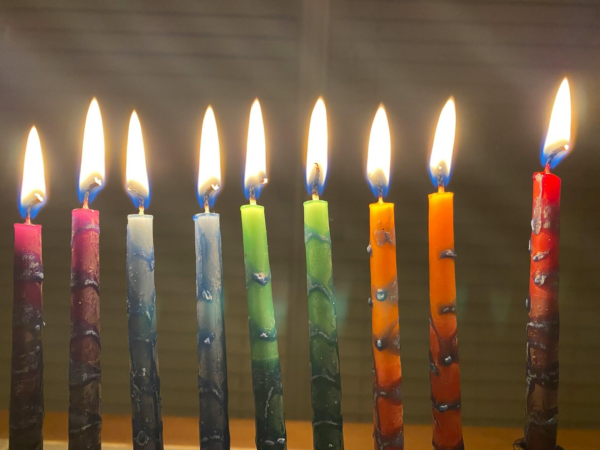 תשעה נרות צבעוניים בעלי להבות בוהקות, מסודרים בשורה על רקע כהה