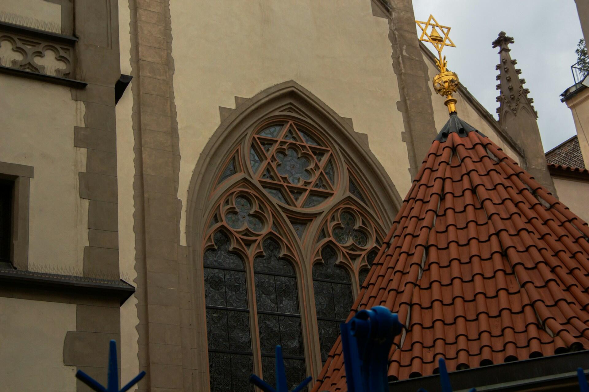 חזית כנסייה גותית עם חלון ויטראז' מורכב, גג רעפים אדומים ועיטור קצה מוזהב ומקושט בצורת מגן דוד