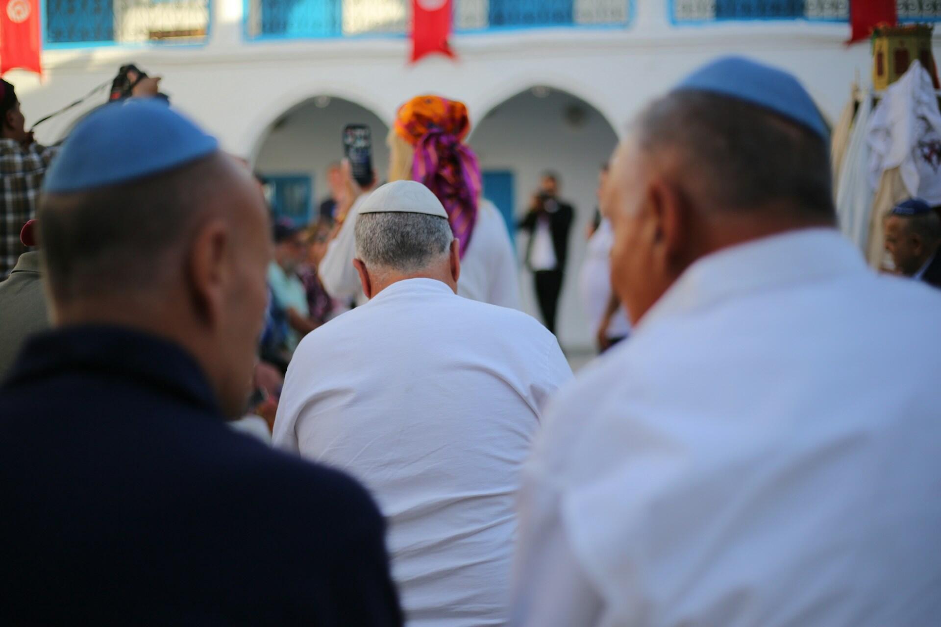 קהל גברים החובשים כובעים כחולים-לבנים מתאסף מחוץ לבניין צבעוני במהלך חגיגה תרבותית או דתית