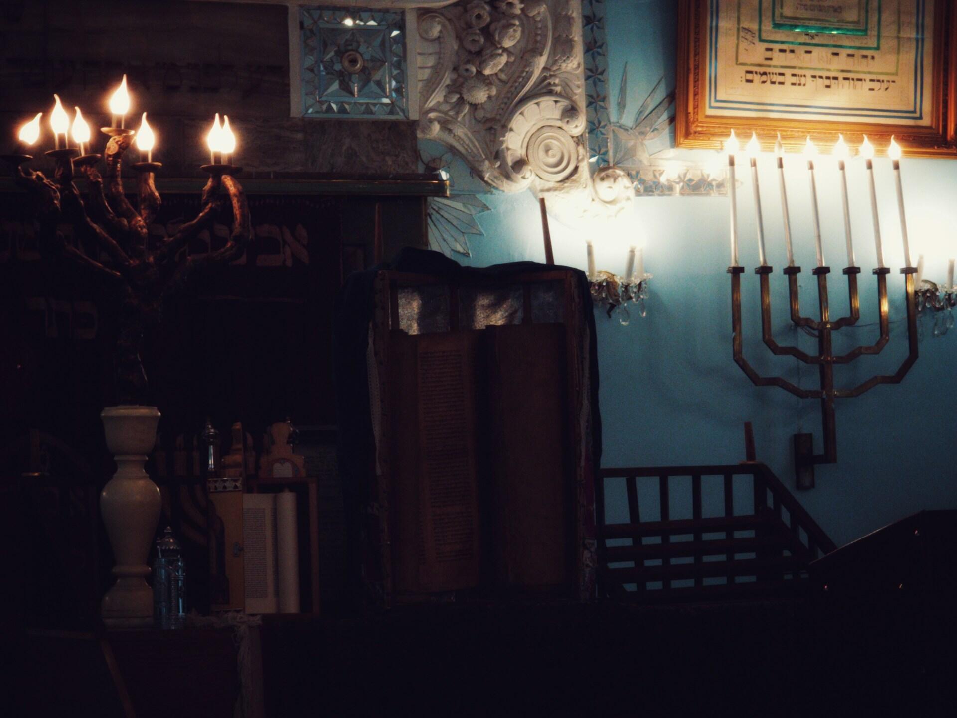 חלל תפילה יהודי מואר בנרות, הכולל מנורות, פסיפסים מעוטרים בגווני כחול ולבן, ארון קודש וכתובות עבריות ממוסגרות