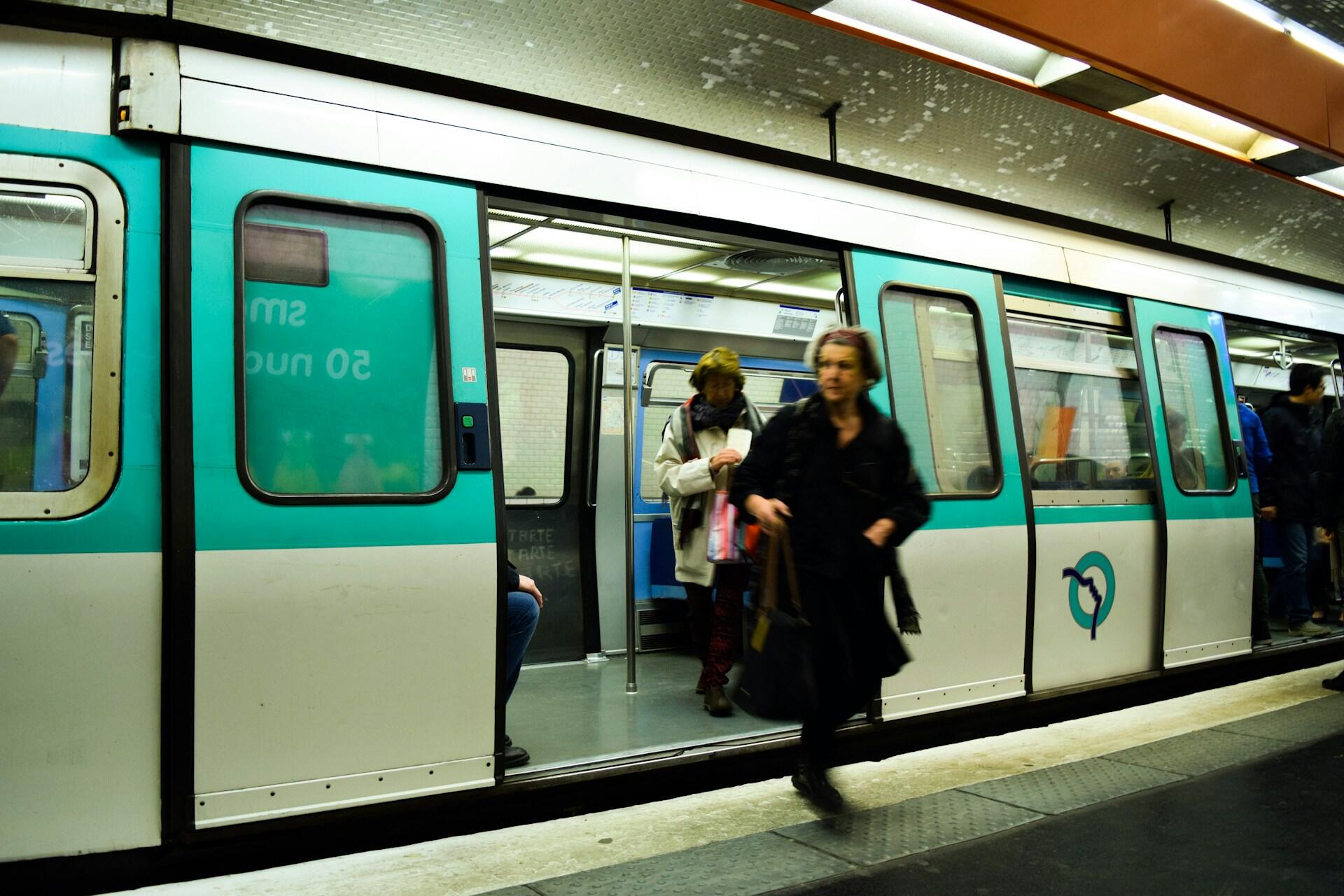 נוסעים עולים לרכבת תחתית בצבע טורקיז ויורדים ממנה בתחנה תת-קרקעית