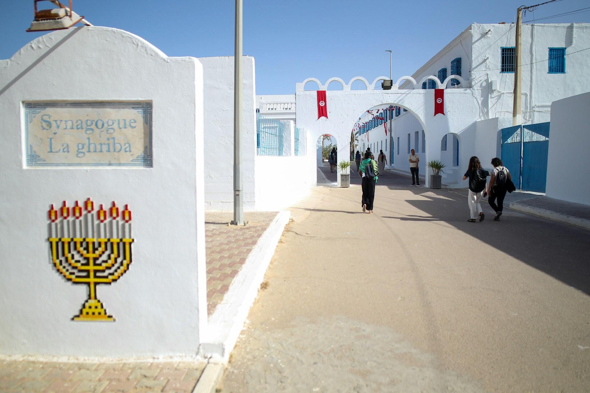 כניסה מסוידת בלבן לבית הכנסת אל-גריבה בג'רבה, המקושטת בדגלי תוניסיה ועוברי אורח פוקדים אותה