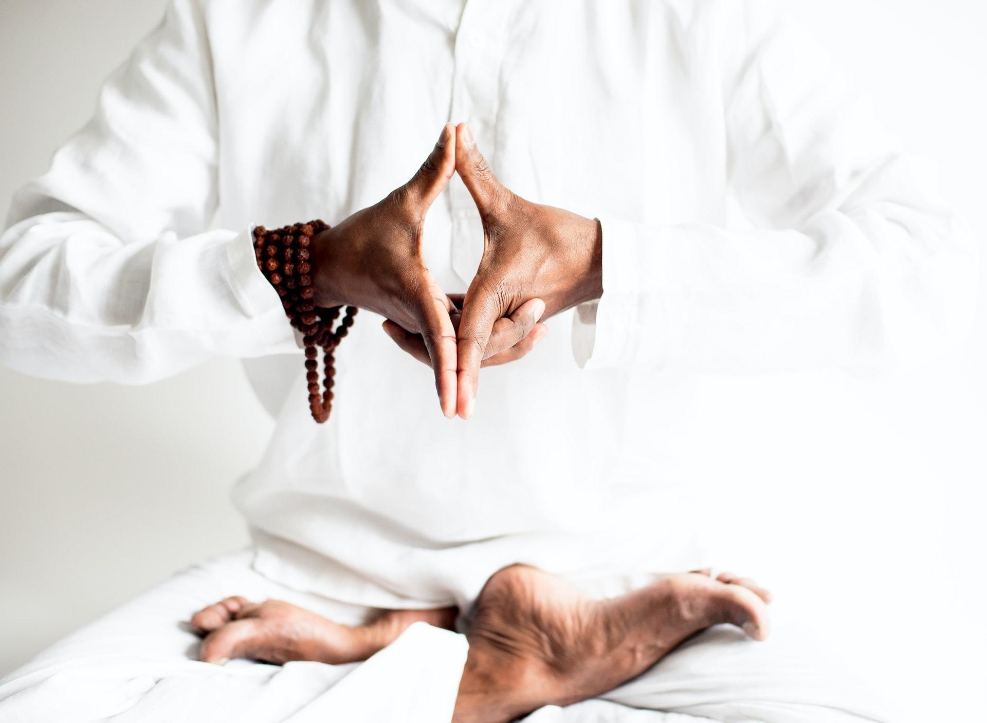 A yogi in all white sitting in lotus pose and a hand mudra.