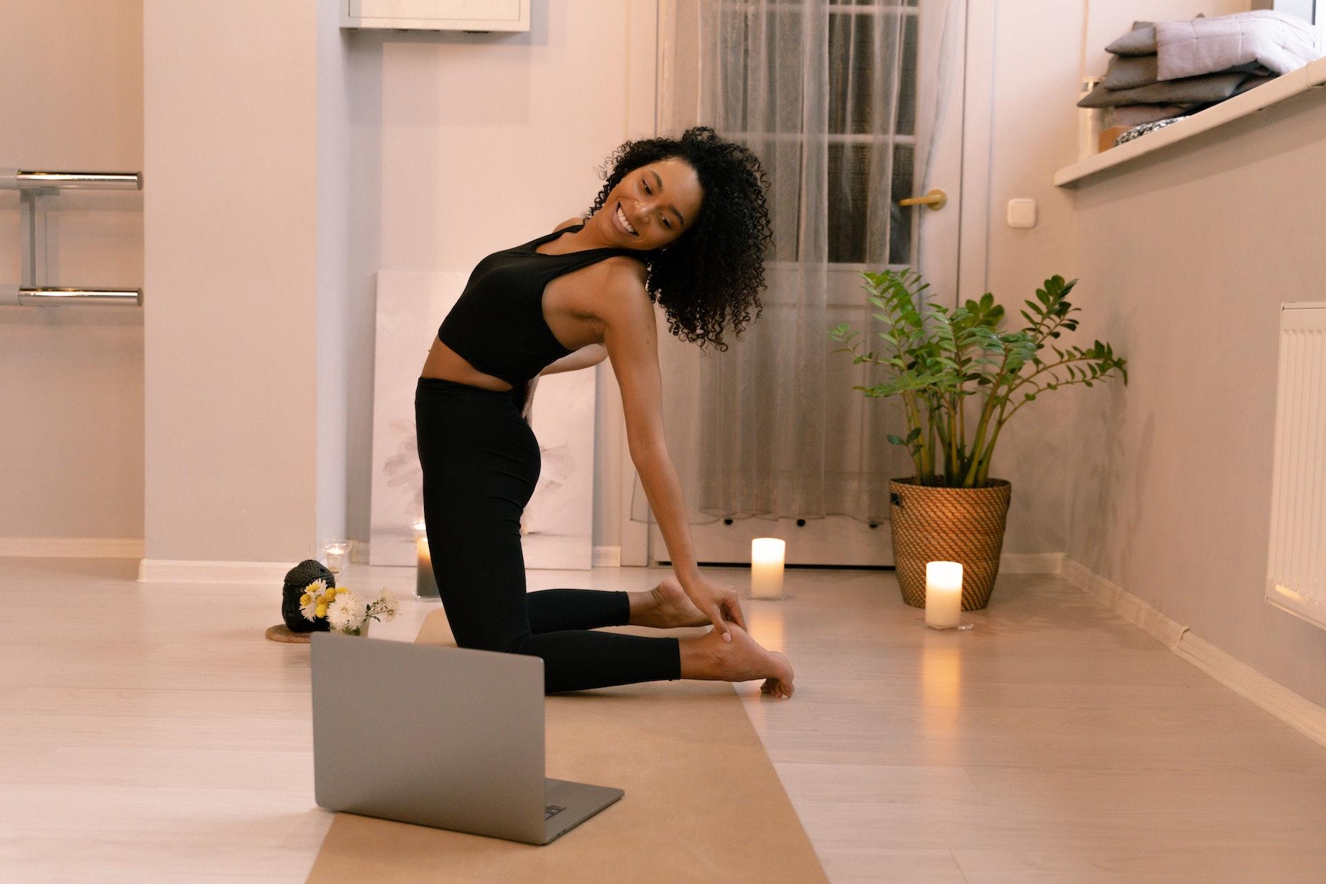 A yogi practices at home while watching a video on their computer.