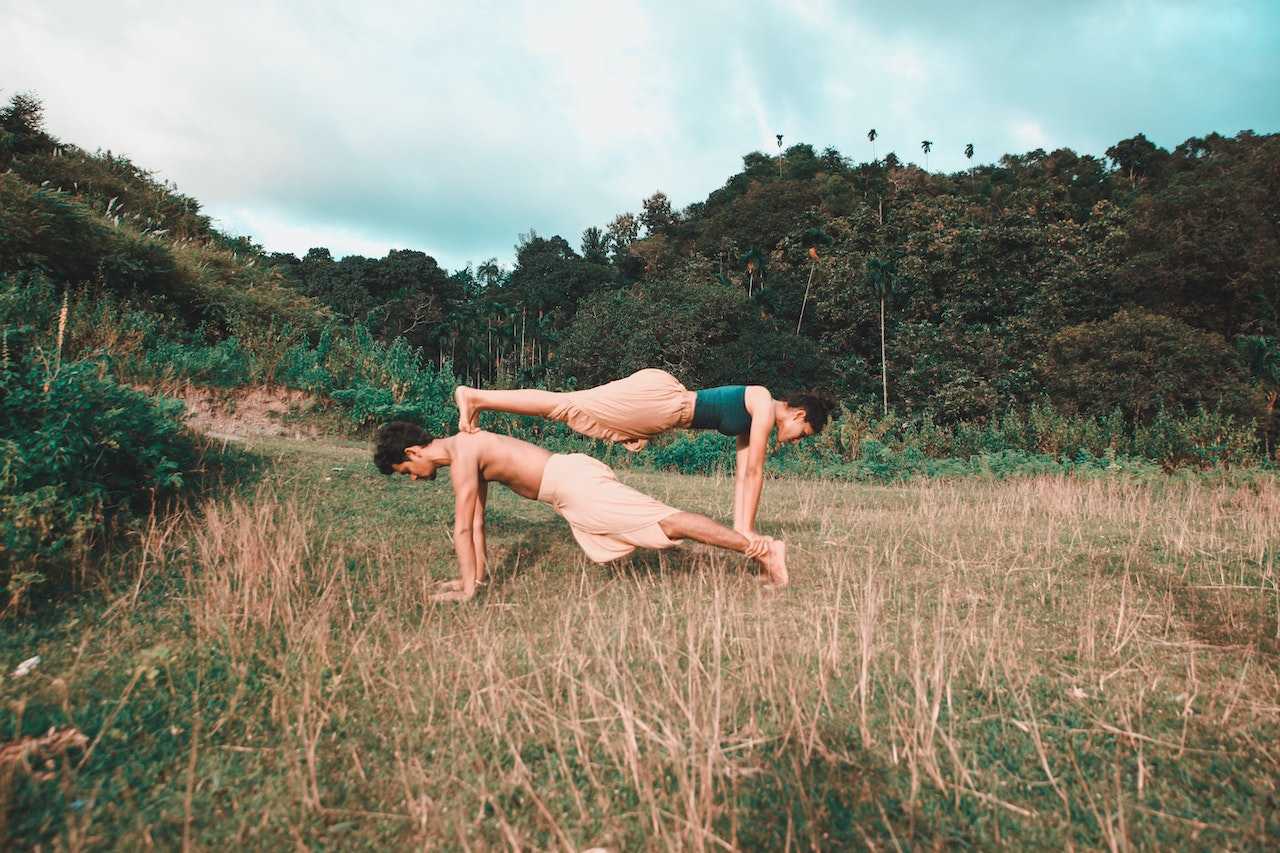 A man and a woman practicing partner yoga. Both are wearing dhotis.