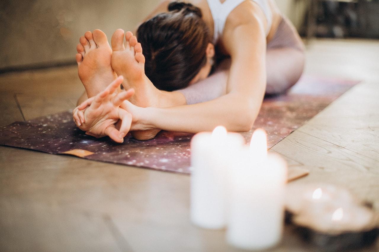 A yogi in Paschimottanasana with a mudra and candles and incense nearby.
