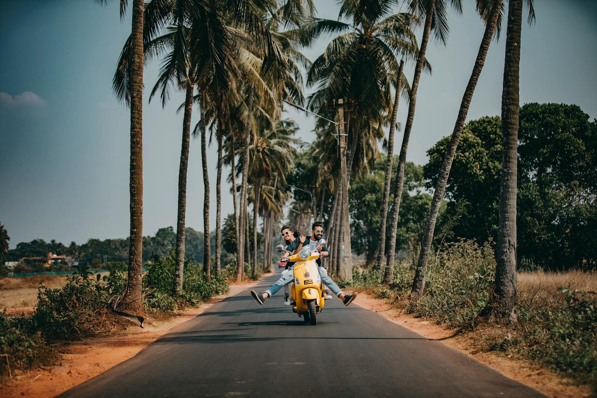 couple riding a scooter on the famous road in Goa lined with palm trees