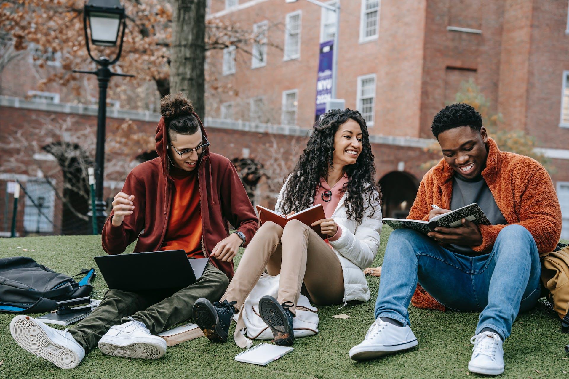 three university students sitting on grass and smiling