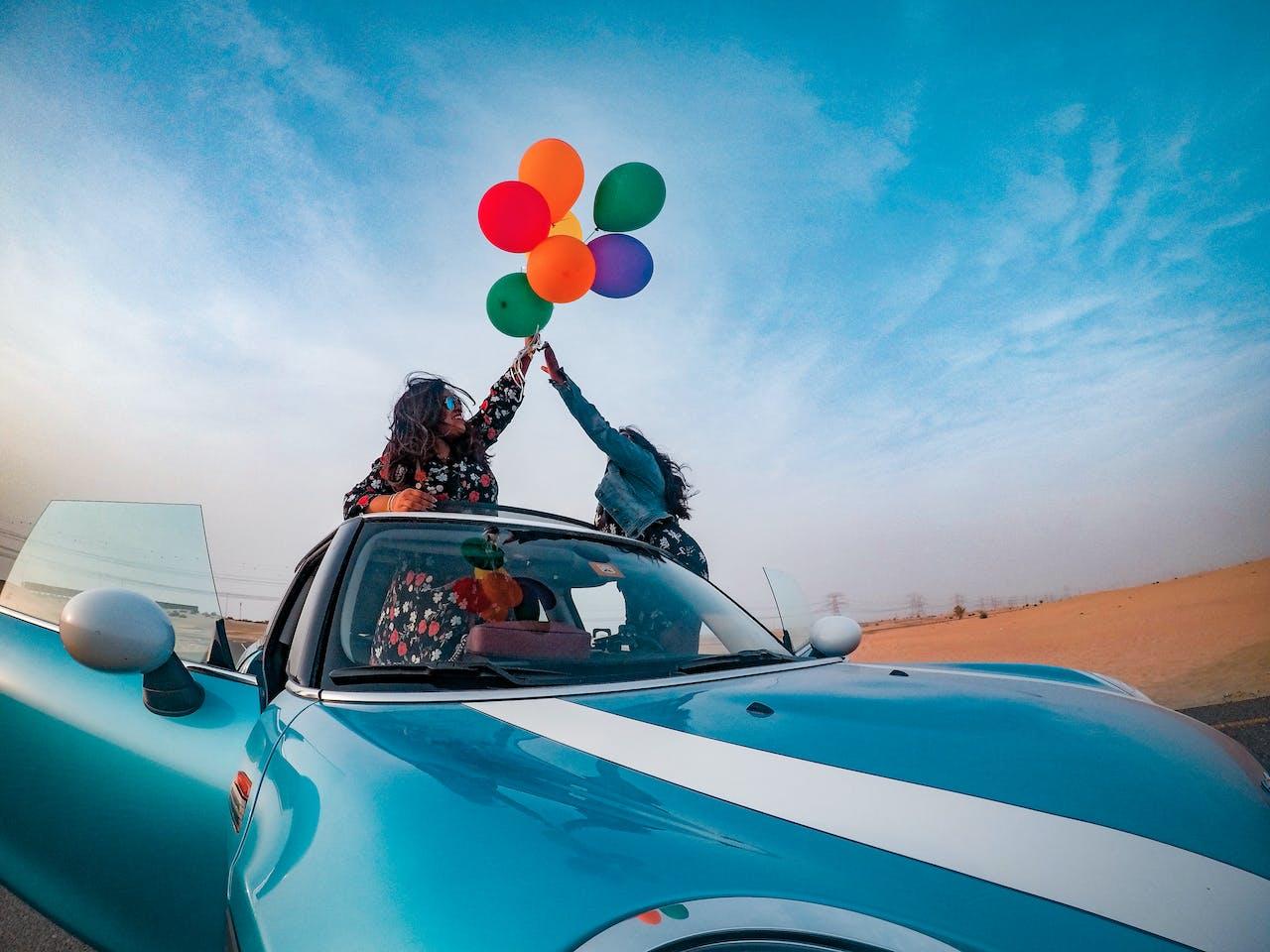 Two girls celebrating a shiny new car with balloons
